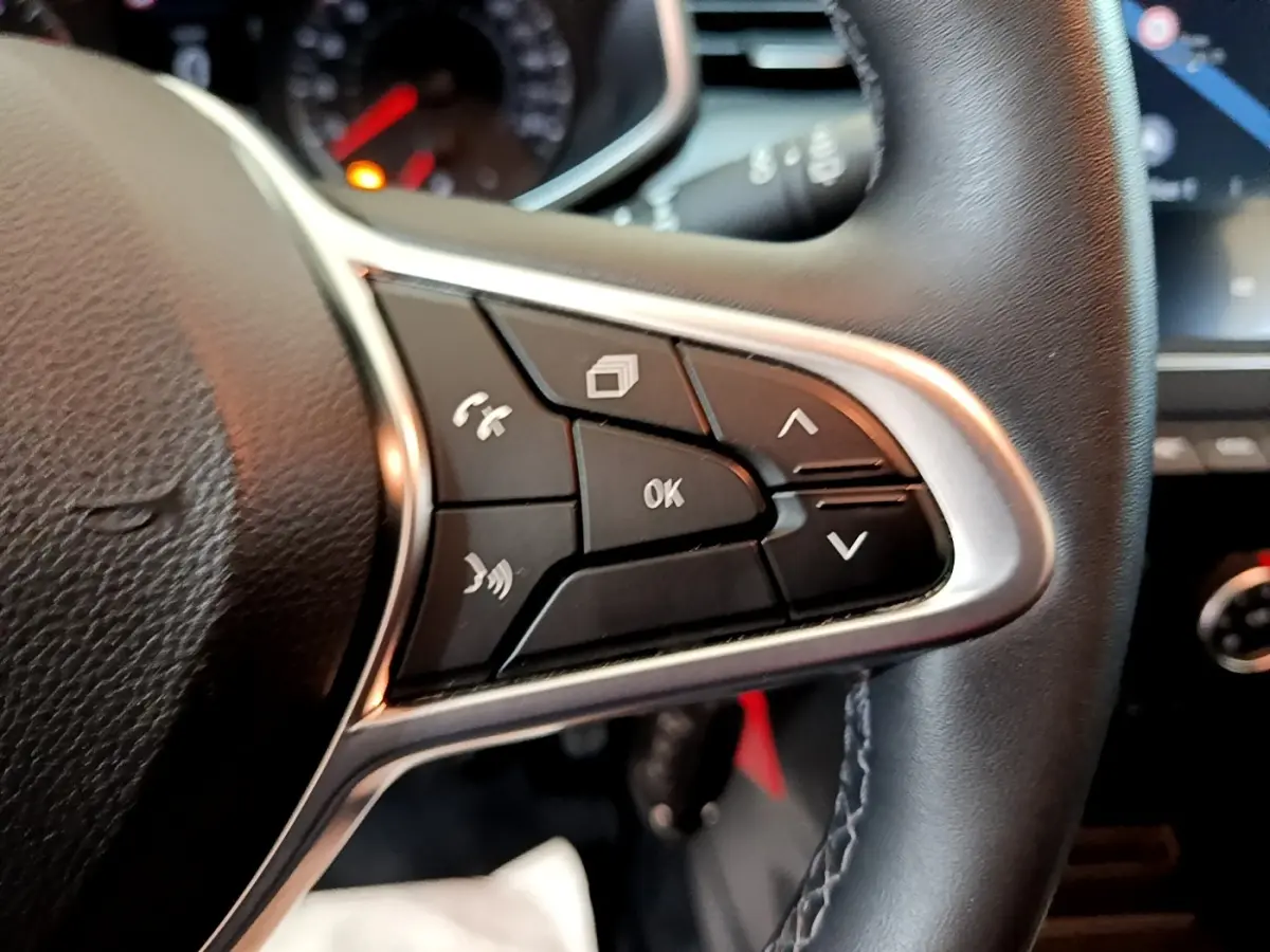 Gros plan sur les commandes multifonctions noires du volant cuir synthétique d'une Renault Clio Business blanc.