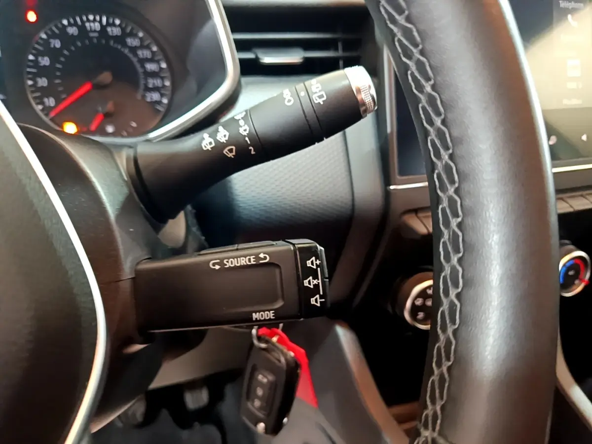 Gros plan sur le volant cuir et les commandes au volant d'une Renault Clio Business blanche, tableau de bord partiellement visible.