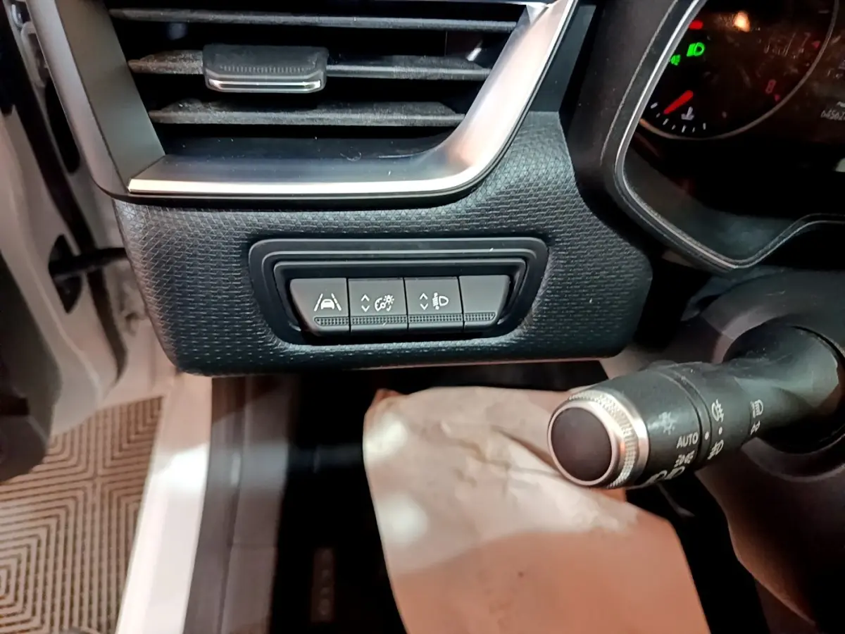 Gros plan sur les commandes d'assistance et réglages d'éclairage à gauche du volant d'une Renault Clio Business blanche de 2019.