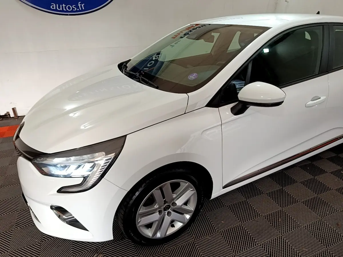 Renault Clio Business TCe 100 blanc vue 3/4 avant droit avec phares LED allumés et jantes alliage.