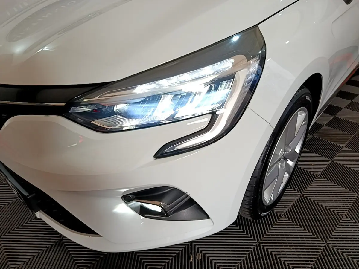 Gros plan sur l'avant droit blanc d'une Renault Clio 2019, mettant en valeur le phare LED allumé et la jante alu.