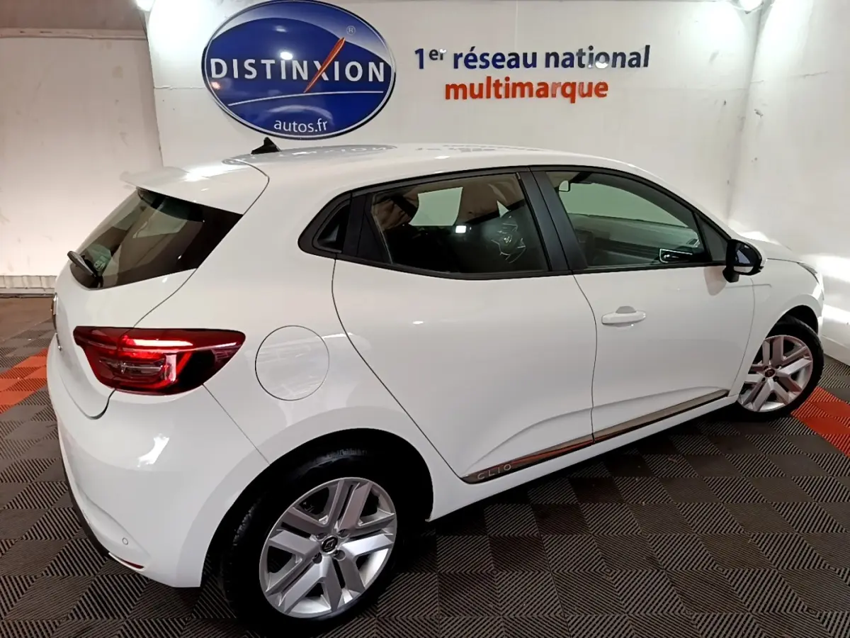 Vue 3/4 arrière droite d'une Renault Clio Business blanche, avec jantes alliage et feux arrière LED allumés.