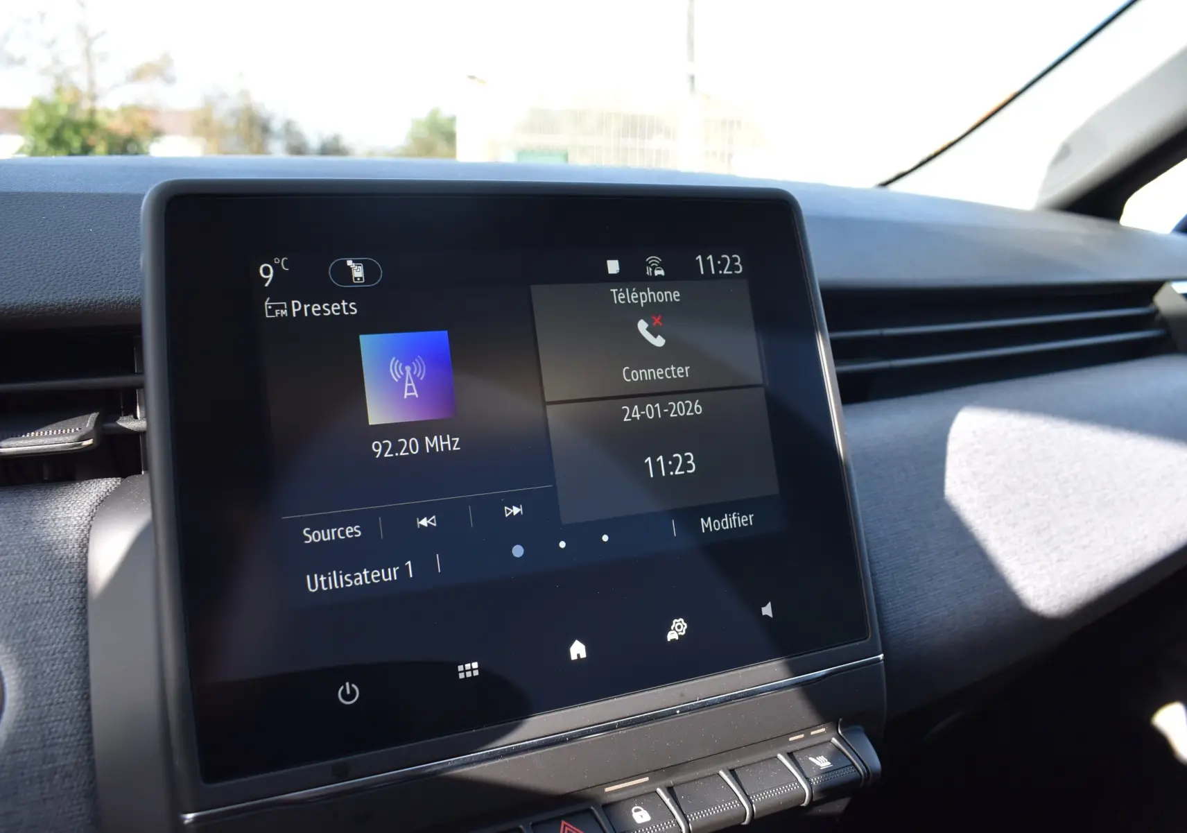 Écran tactile central de la Renault Clio V noir, affichant la radio FM et la connexion téléphone, vue intérieure avant.