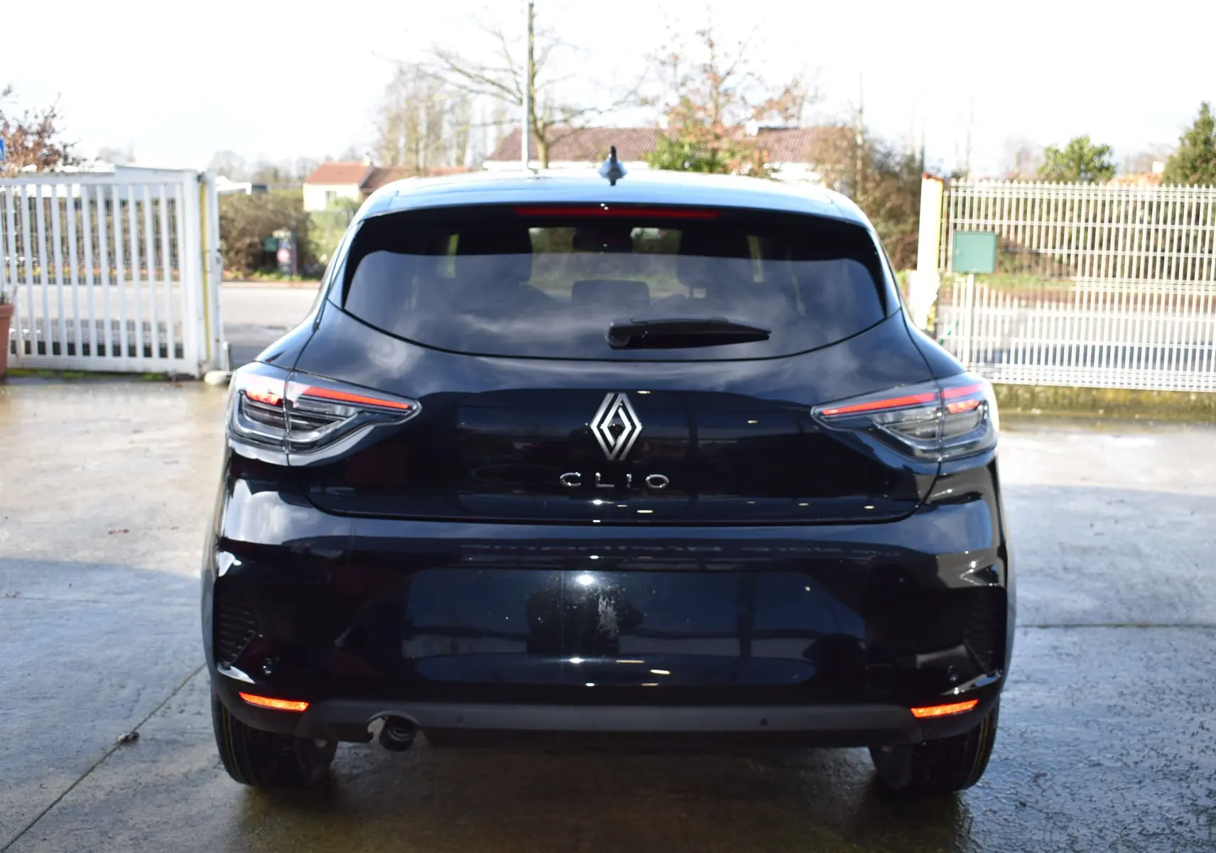 Vue arrière d'une Renault Clio V noire 2025 avec feux LED et hayon fermé sur un sol mouillé.