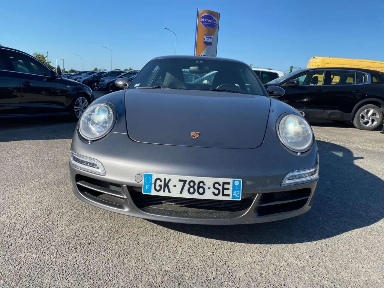 Vue avant d'une Porsche 911 Carrera 4S gris météore stationnée en extérieur sous un ciel bleu.
