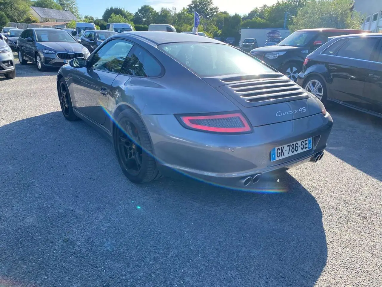 Vue 3/4 arrière droite d'une Porsche 911 Carrera 4S gris météore avec jantes noires et double sortie d'échappement.