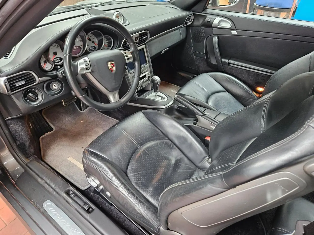 Vue intérieure côté conducteur de la Porsche 911 Carrera 4S 2007 avec sièges sport cuir noir et volant multifonction.