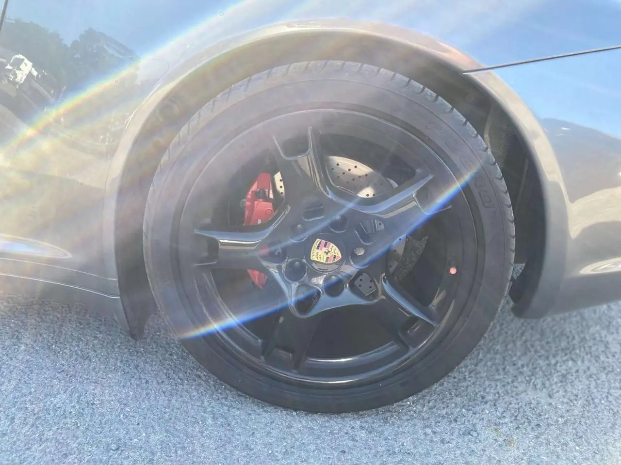 Gros plan sur la jante noire Carrera Sport 19 pouces avec étrier de frein rouge sur Porsche 911 gris météore côté arrière droit.