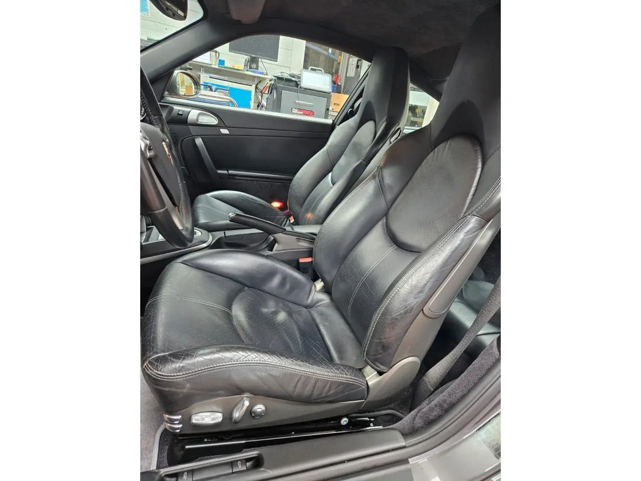 Vue intérieure côté conducteur de la Porsche 911 Carrera 4S 2007 avec sièges sport cuir noir et volant multifonction.