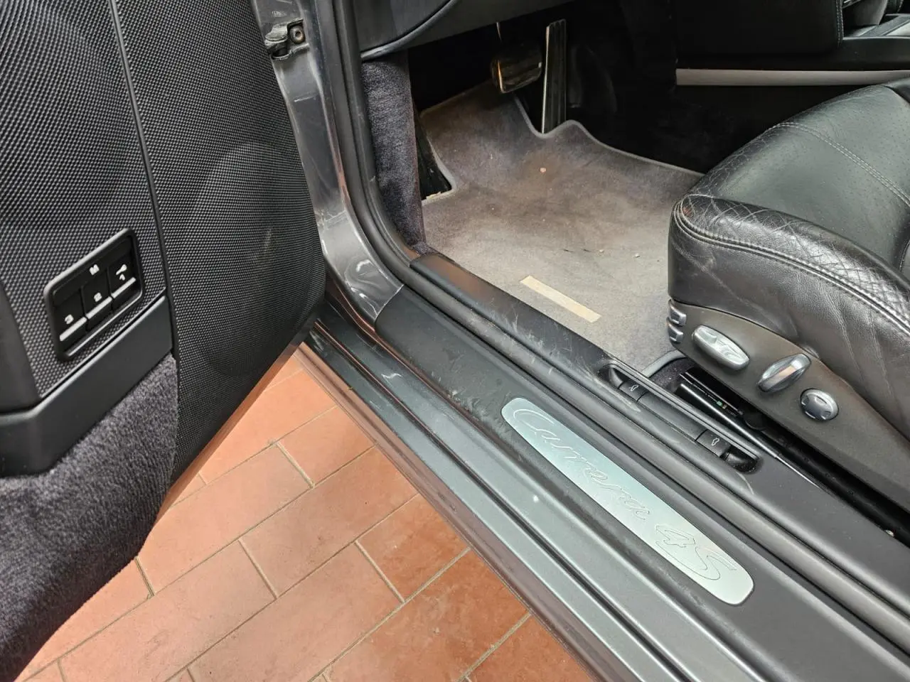 Vue intérieure côté conducteur de la Porsche 911 Carrera 4S 2007 gris météore, siège cuir noir et seuil de porte Carrera 4S.