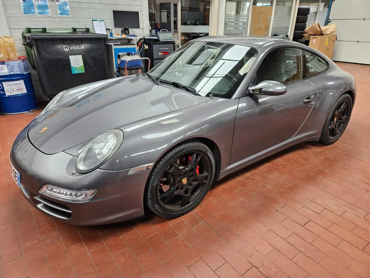 Porsche 911 Carrera 4S gris météore vue 3/4 avant droit, jantes noires Carrera Sport 19 pouces et freins rouges visibles.