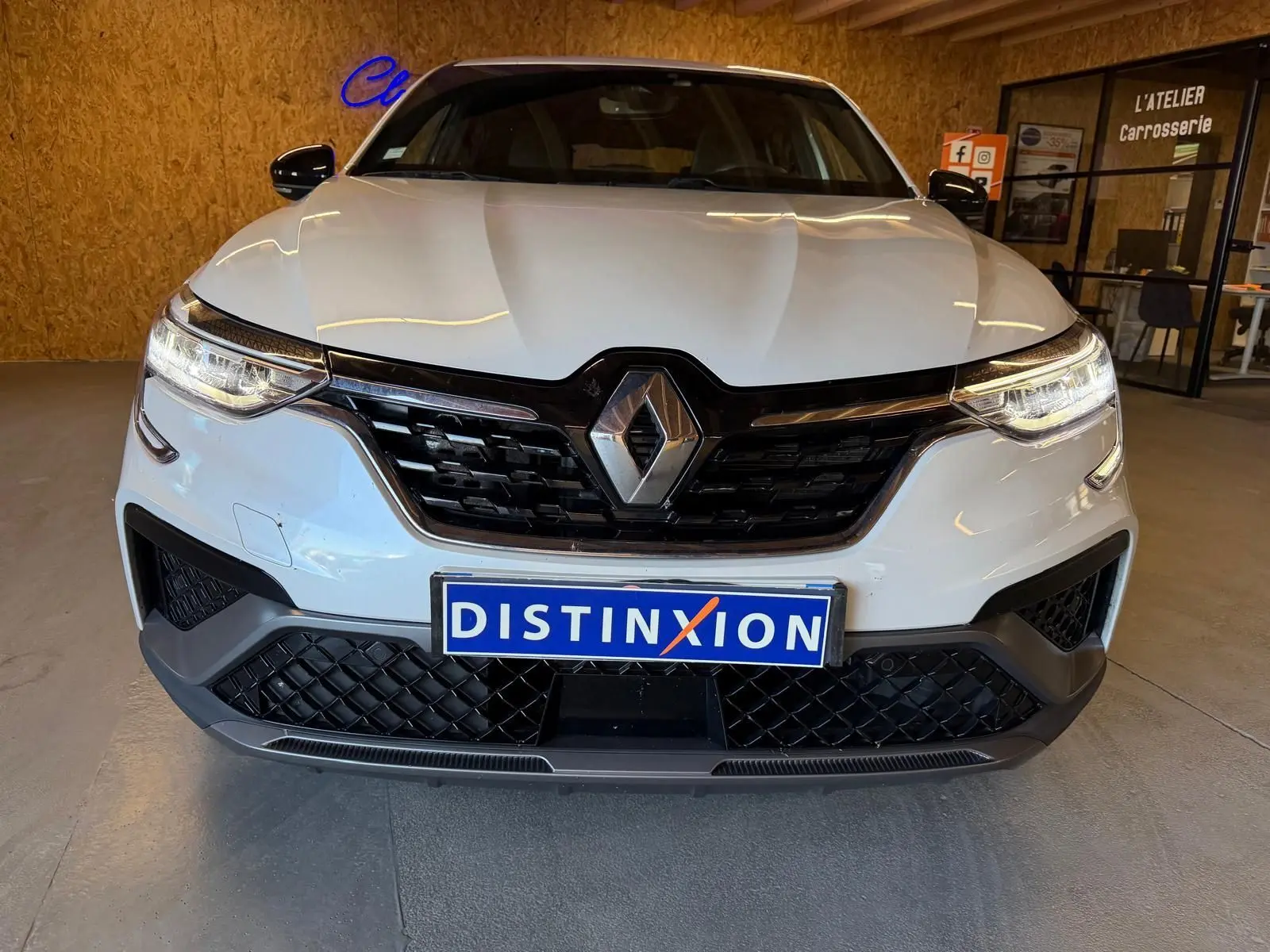 Vue avant d'un Renault Arkana blanc nacré avec calandre noire et phares LED allumés en intérieur showroom.