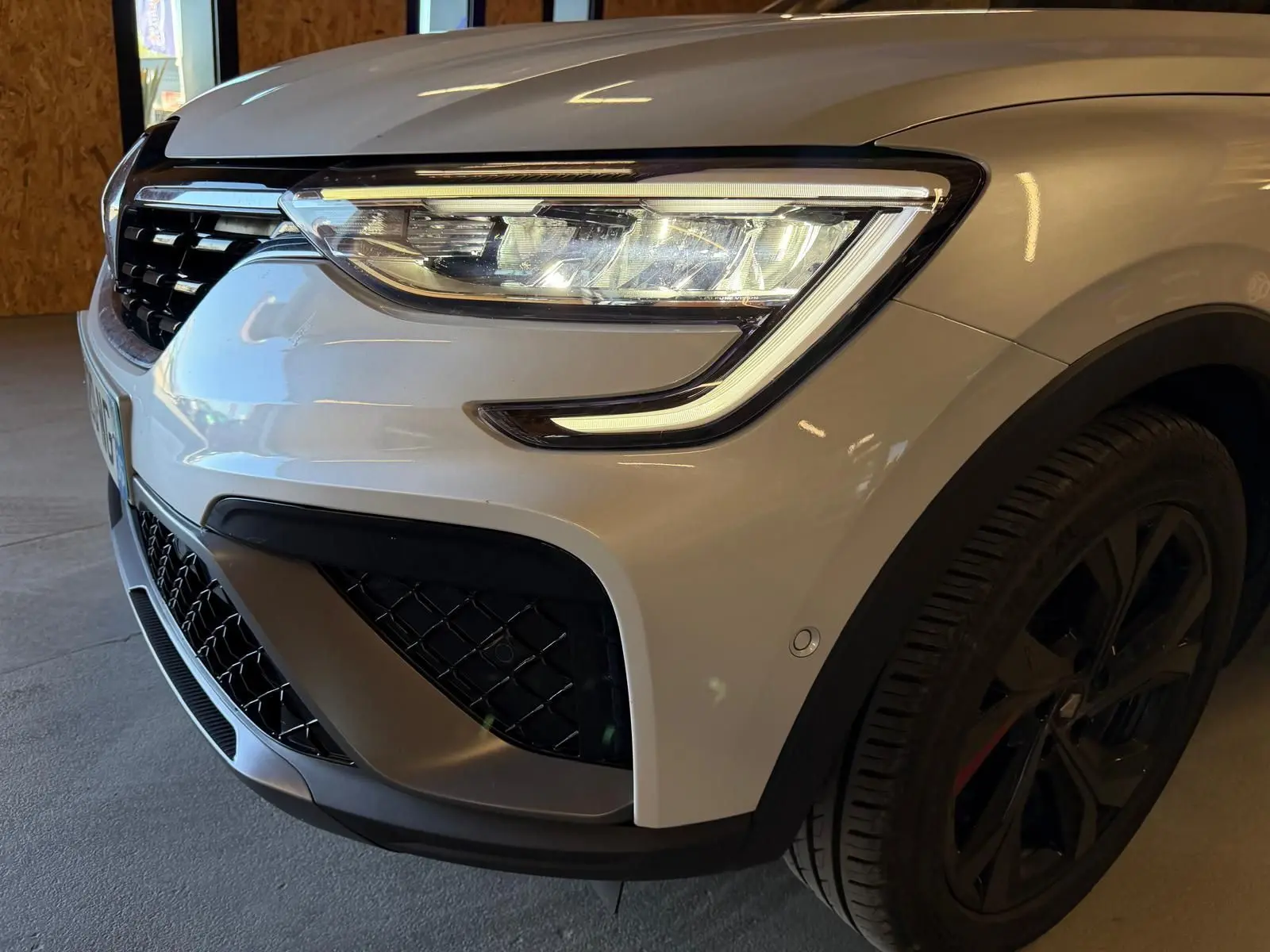 Gros plan sur l'avant droit blanc nacré du Renault Arkana 1.6 E-Tech hybrid 145 RS LINE avec phares LED et jante alu noire.