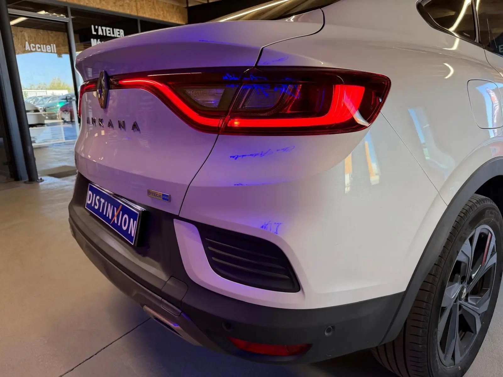 Vue 3/4 arrière droite d'un Renault Arkana blanc nacré avec feux LED allumés et jantes alu noires.