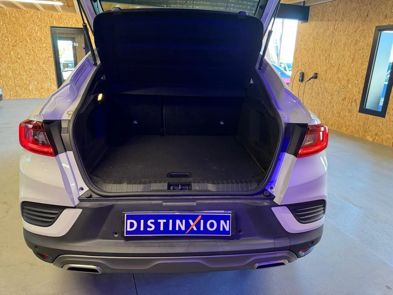 Vue arrière d'un Renault Arkana blanc nacré avec coffre ouvert et sorties d'échappement chromées visibles en intérieur.