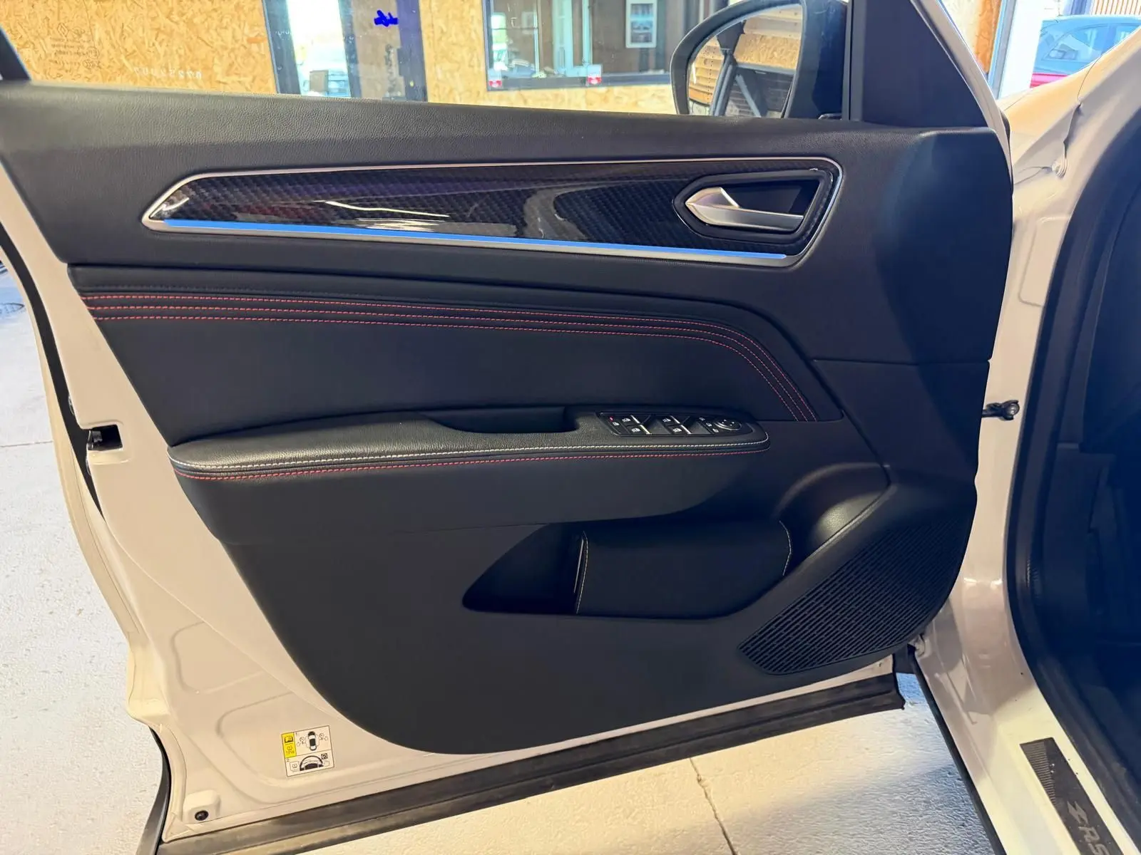 Vue rapprochée de la porte avant gauche blanche nacrée du Renault Arkana 1.6 E-Tech RS Line avec surpiqûres rouges et insert carbone.