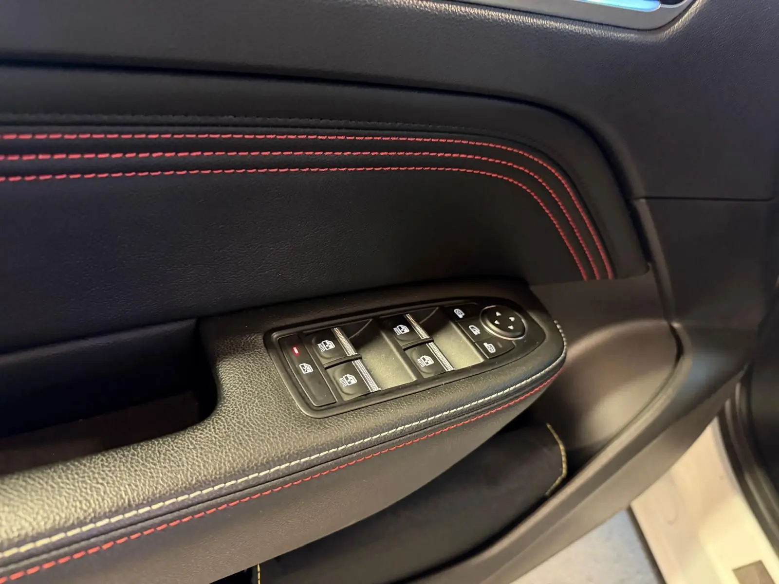 Gros plan sur la commande des vitres électriques côté gauche avec surpiqûres rouges sur garniture noire du Renault Arkana blanc nacré.