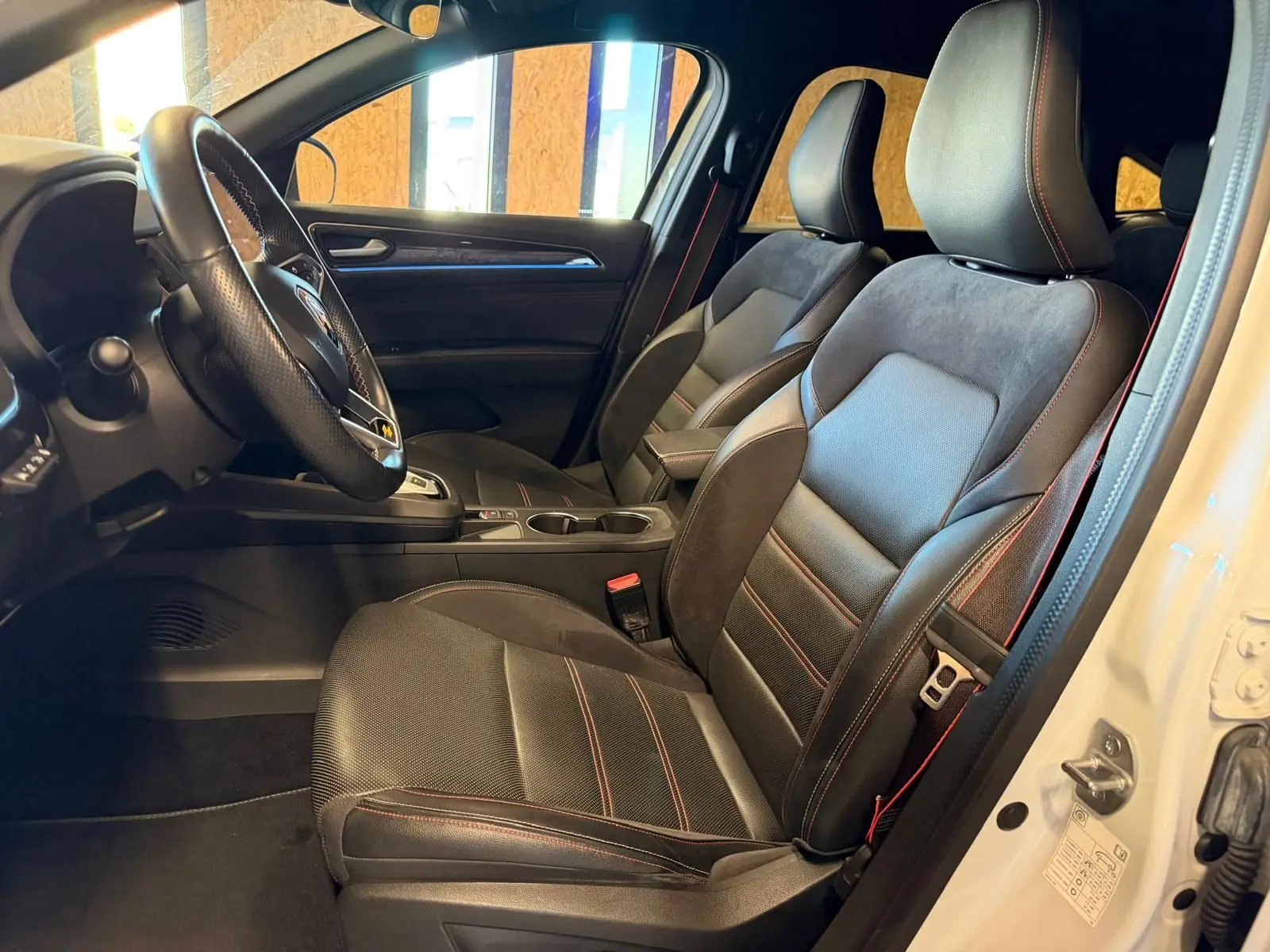 Vue intérieure côté conducteur du Renault Arkana blanc nacré, sièges sport noir avec surpiqûres rouges et volant cuir multifonctions.