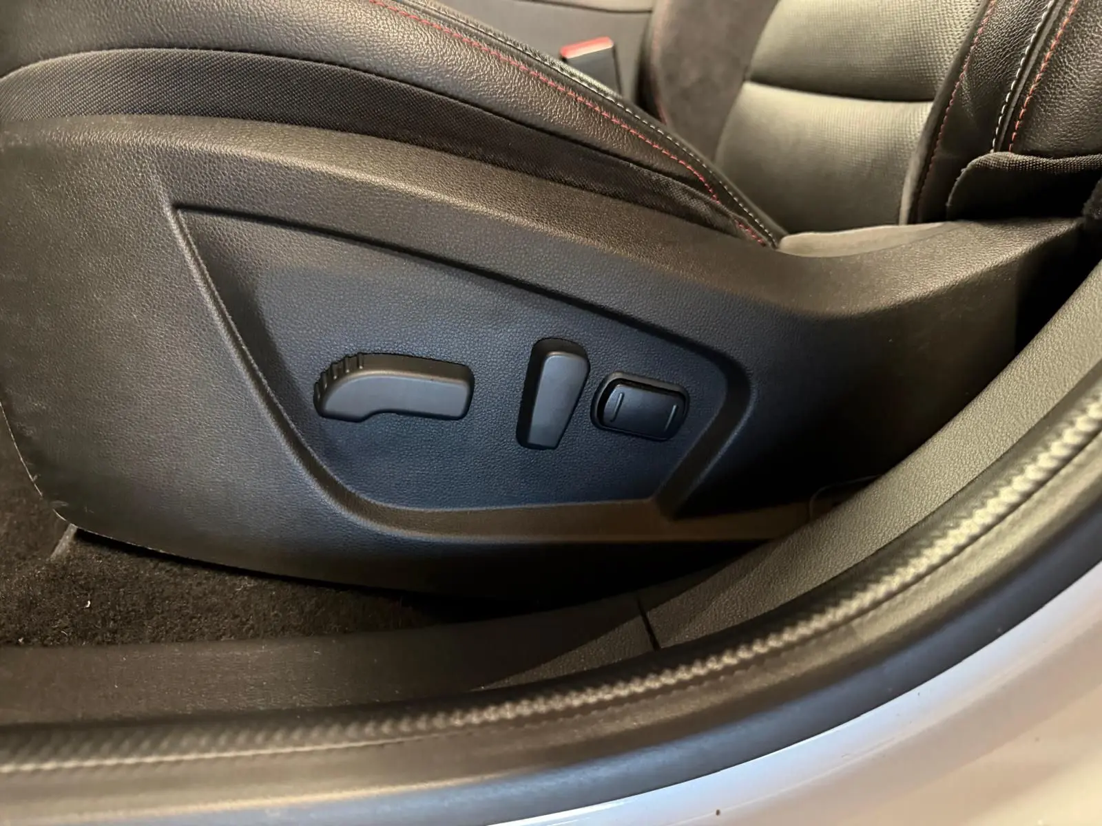 Gros plan sur les commandes électriques du siège conducteur noir avec surpiqûres rouges dans Renault Arkana blanc nacré.