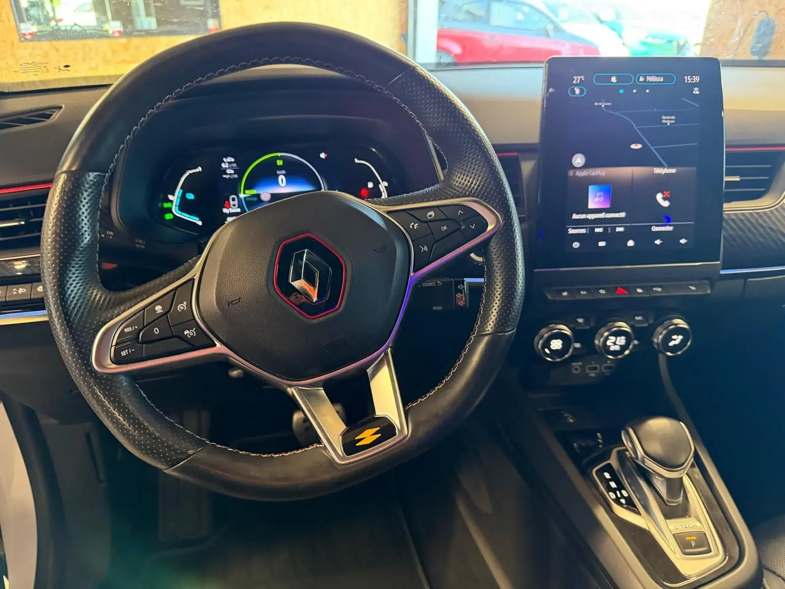 Vue intérieure centrée sur le volant noir avec logo Renault rouge, tableau de bord digital et écran tactile vertical.