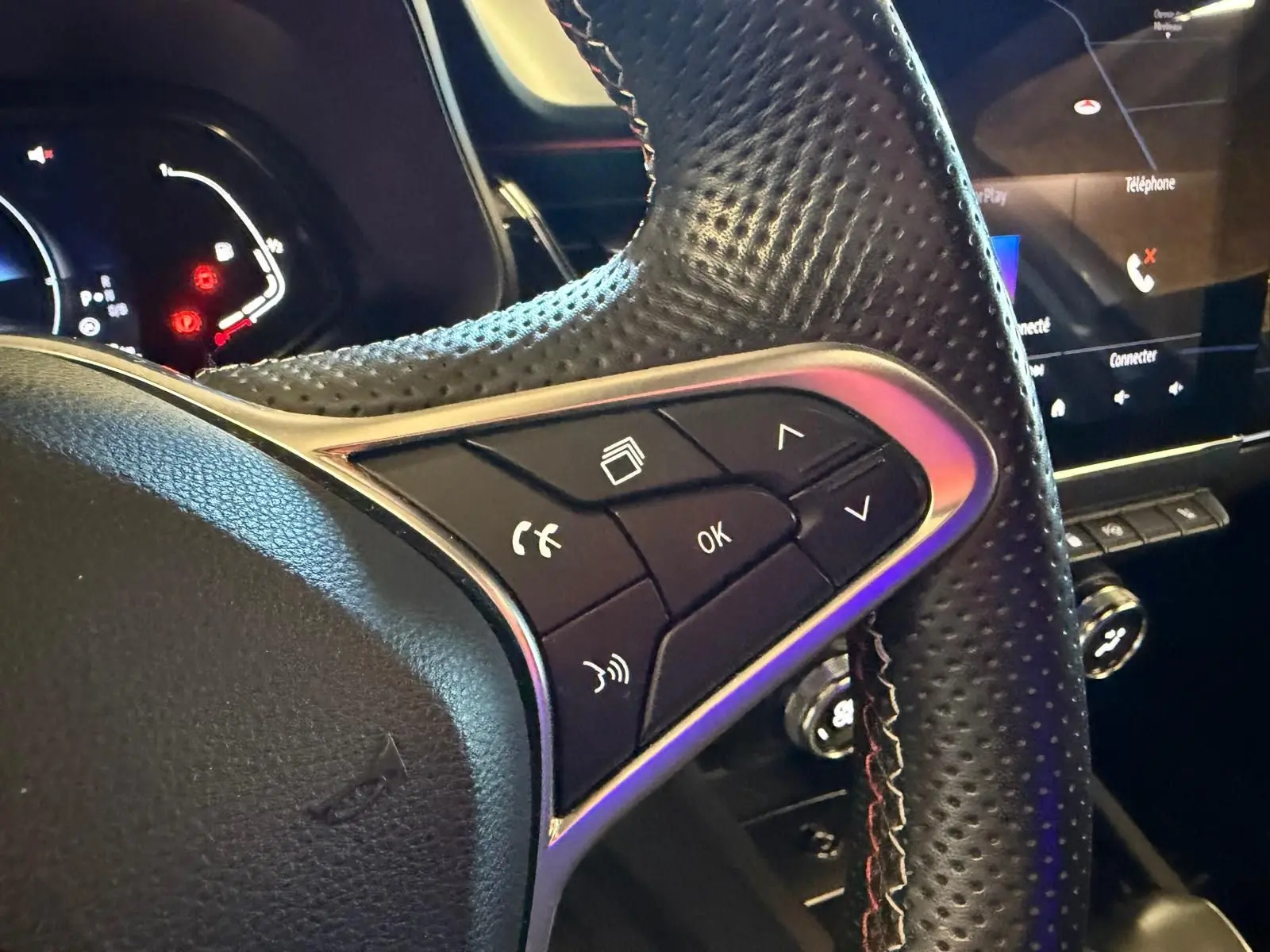 Gros plan sur le volant cuir perforé côté gauche du Renault Arkana blanc nacré avec commandes multifonctions visibles.