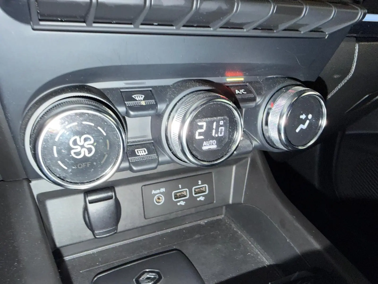 Gros plan sur la console centrale noire du Renault Arkana 1.6 E-Tech hybrid avec commandes de climatisation et ports USB visibles.