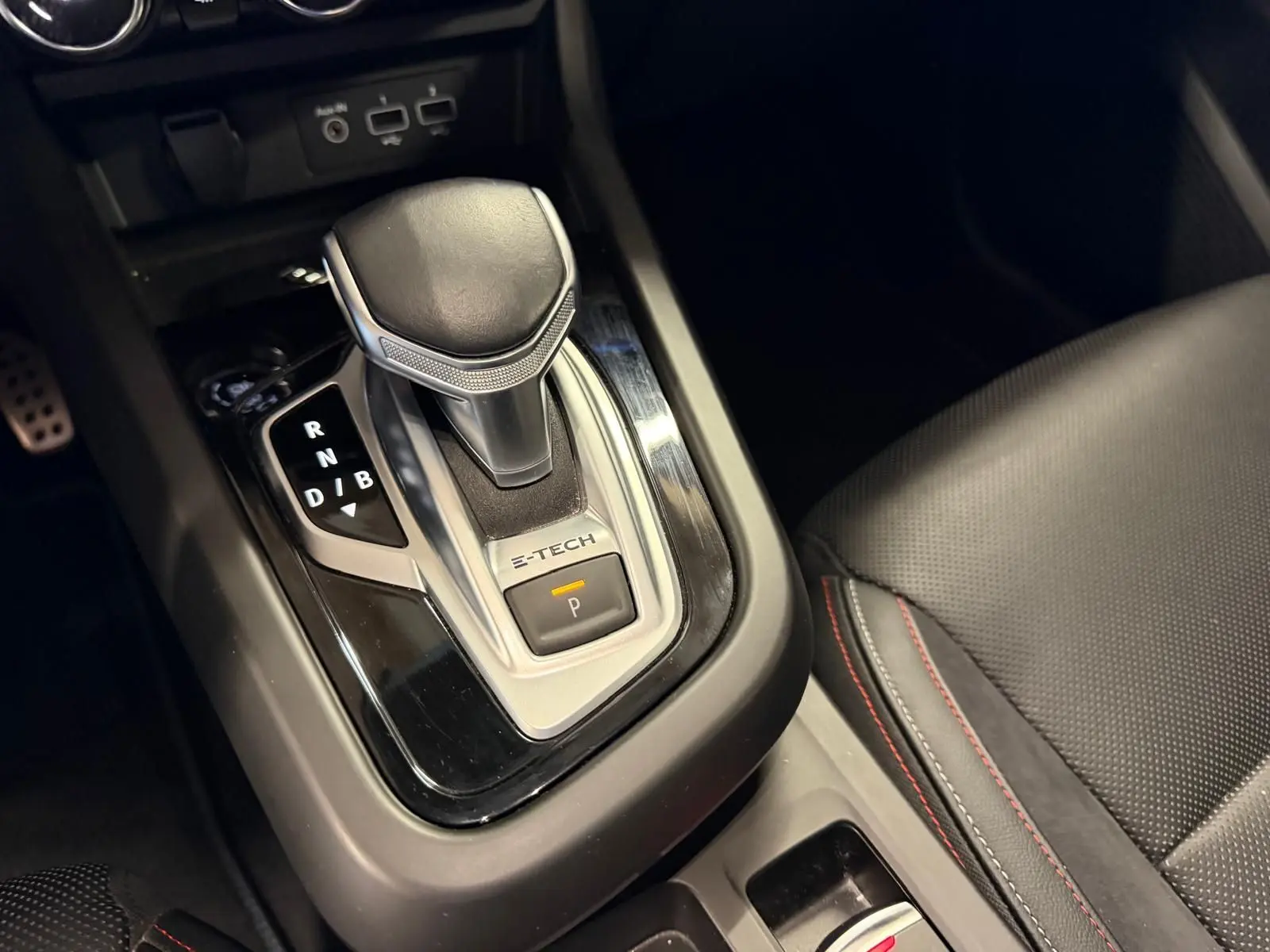 Gros plan sur le levier de vitesse automatique noir et argenté avec inscription E-TECH dans l’habitacle du Renault Arkana blanc nacré.