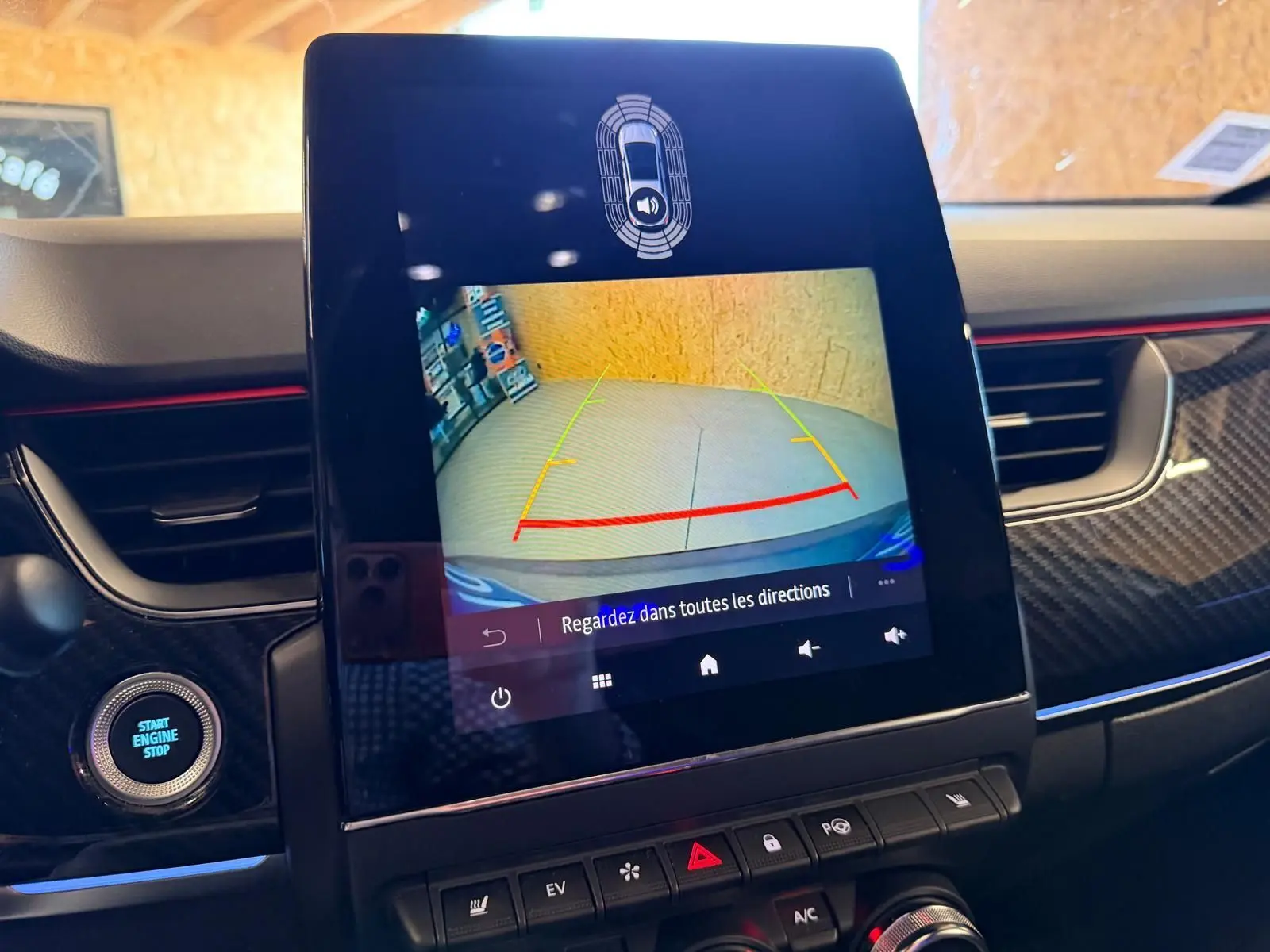 Écran tactile central montrant la caméra de recul, intérieur noir avec détails carbone et bande rouge sur tableau de bord.
