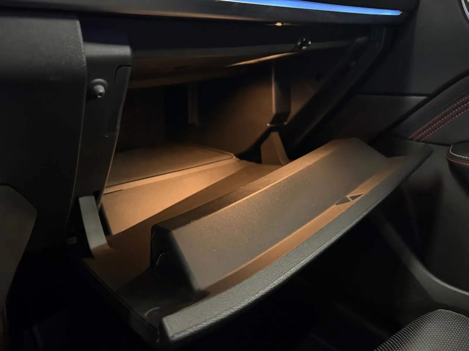 Gros plan sur la boîte à gants ouverte de la Renault Arkana 1.6 E-Tech blanc nacré, intérieur noir avec surpiqûres rouges.