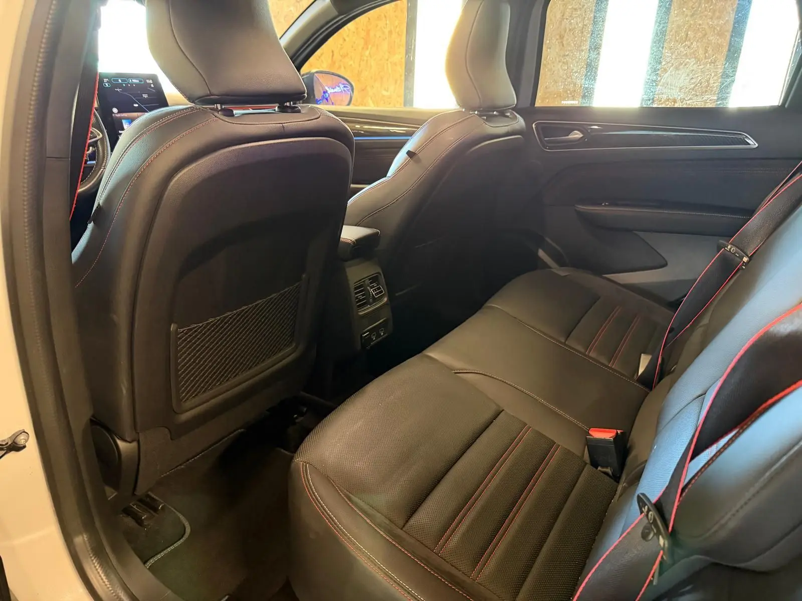 Vue intérieure arrière côté droit du Renault Arkana blanc nacré, sièges cuir noir avec surpiqûres rouges et console centrale.