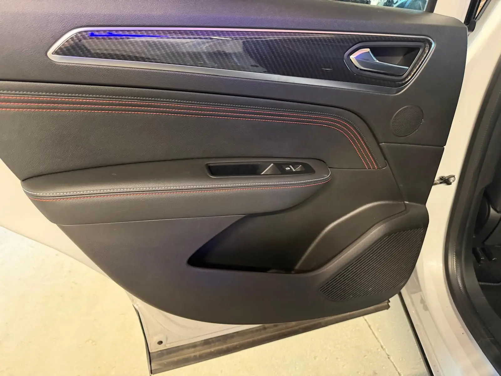 Vue intérieure côté gauche de la porte avant blanche nacrée du Renault Arkana avec surpiqûres rouges et insert carbone.