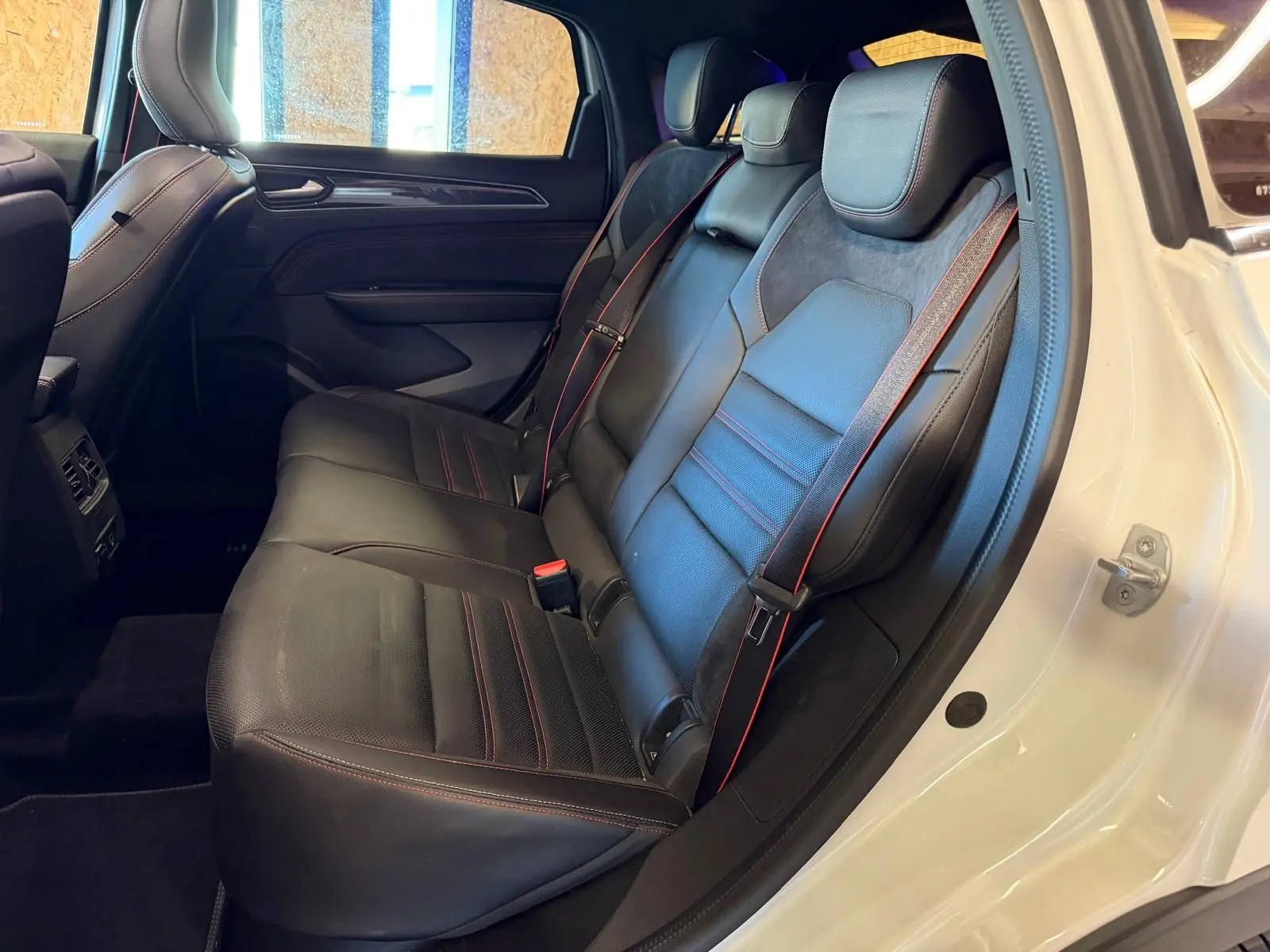Vue intérieure côté gauche des sièges arrière noirs en cuir et suédine avec surpiqûres rouges d'un Renault Arkana blanc nacré.
