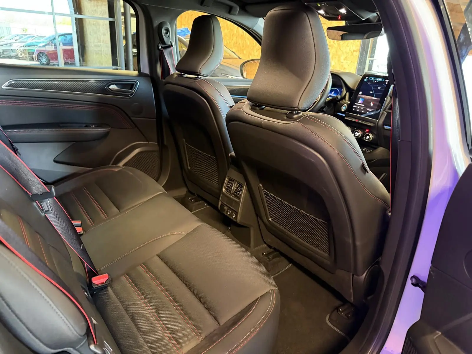 Vue intérieure arrière côté droit du Renault Arkana blanc nacré, sièges sport noirs avec surpiqûres rouges et écran tactile visible.