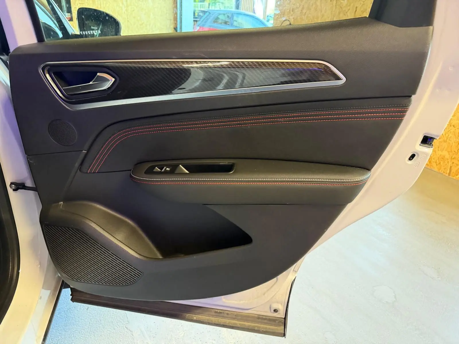 Vue intérieure de la porte arrière droite blanche nacrée du Renault Arkana 1.6 E-Tech avec surpiqûres rouges et insert carbone.