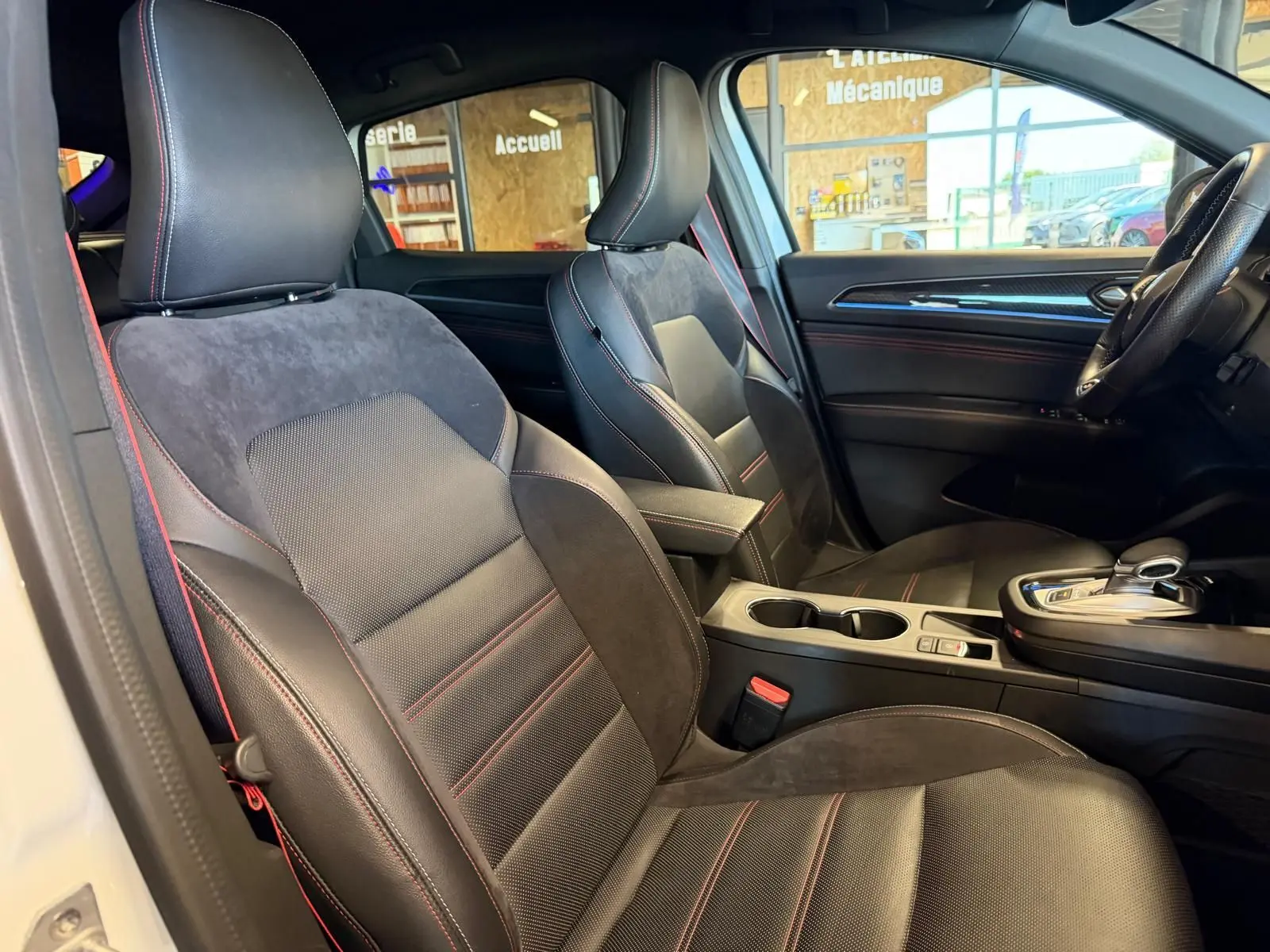 Vue intérieure côté conducteur de la Renault Arkana blanc nacré, sièges sport noirs avec surpiqûres rouges et console centrale.