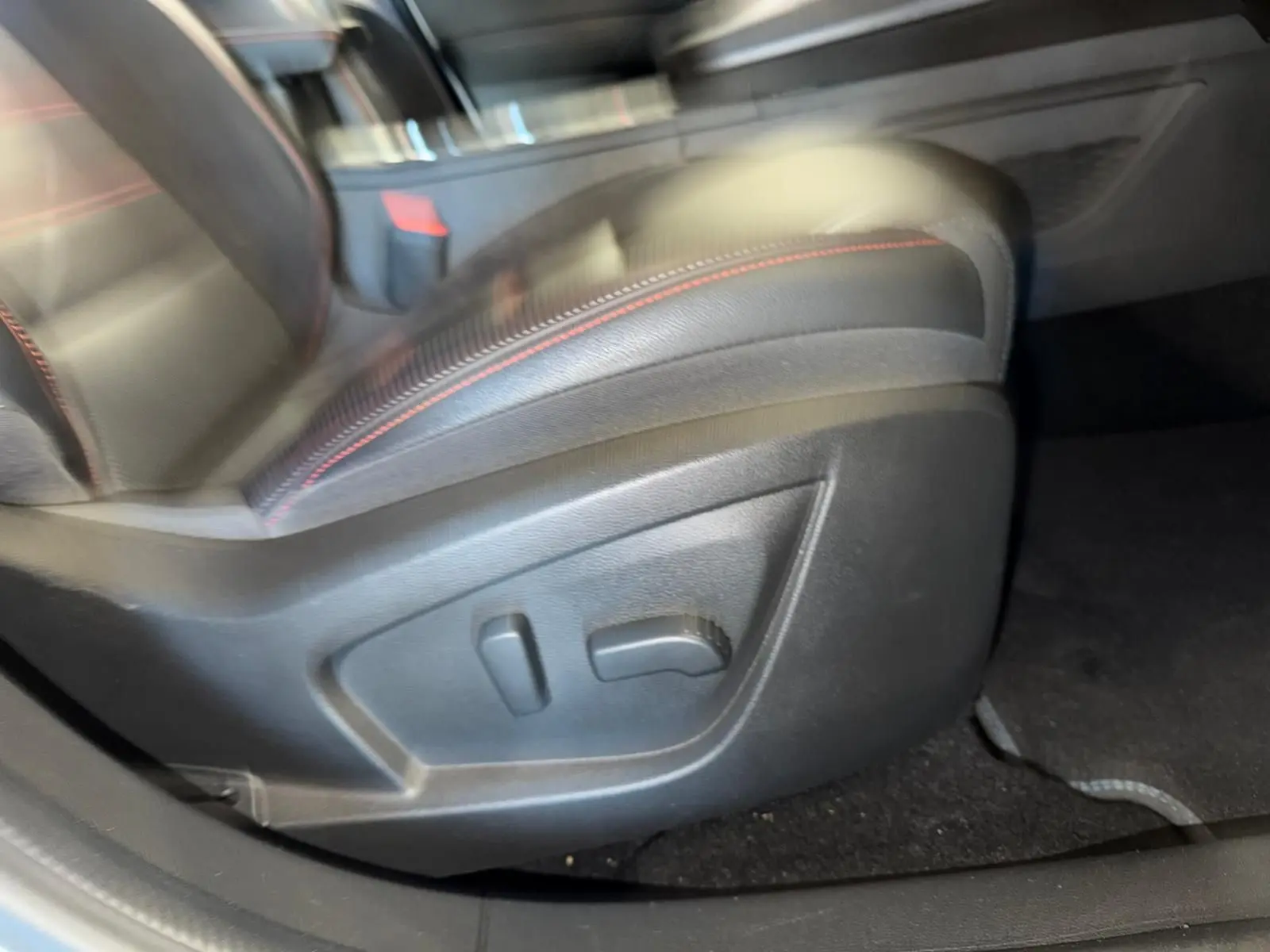 Gros plan sur le réglage électrique du siège conducteur en cuir noir avec surpiqûres rouges dans Renault Arkana blanc nacré.