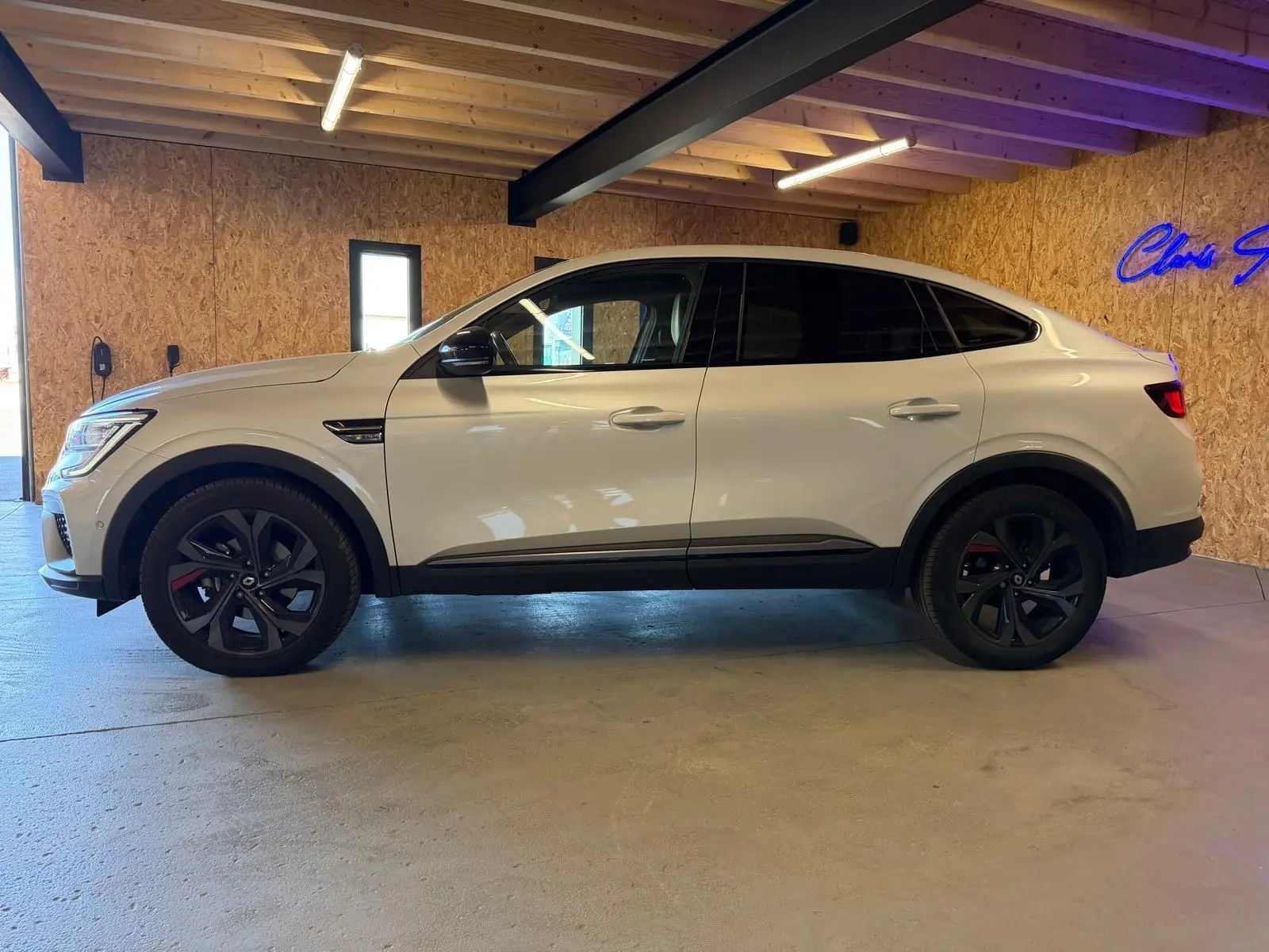 Renault Arkana blanc nacré en profil droit, jantes noires, avec toit incliné et détails RS Line visibles.