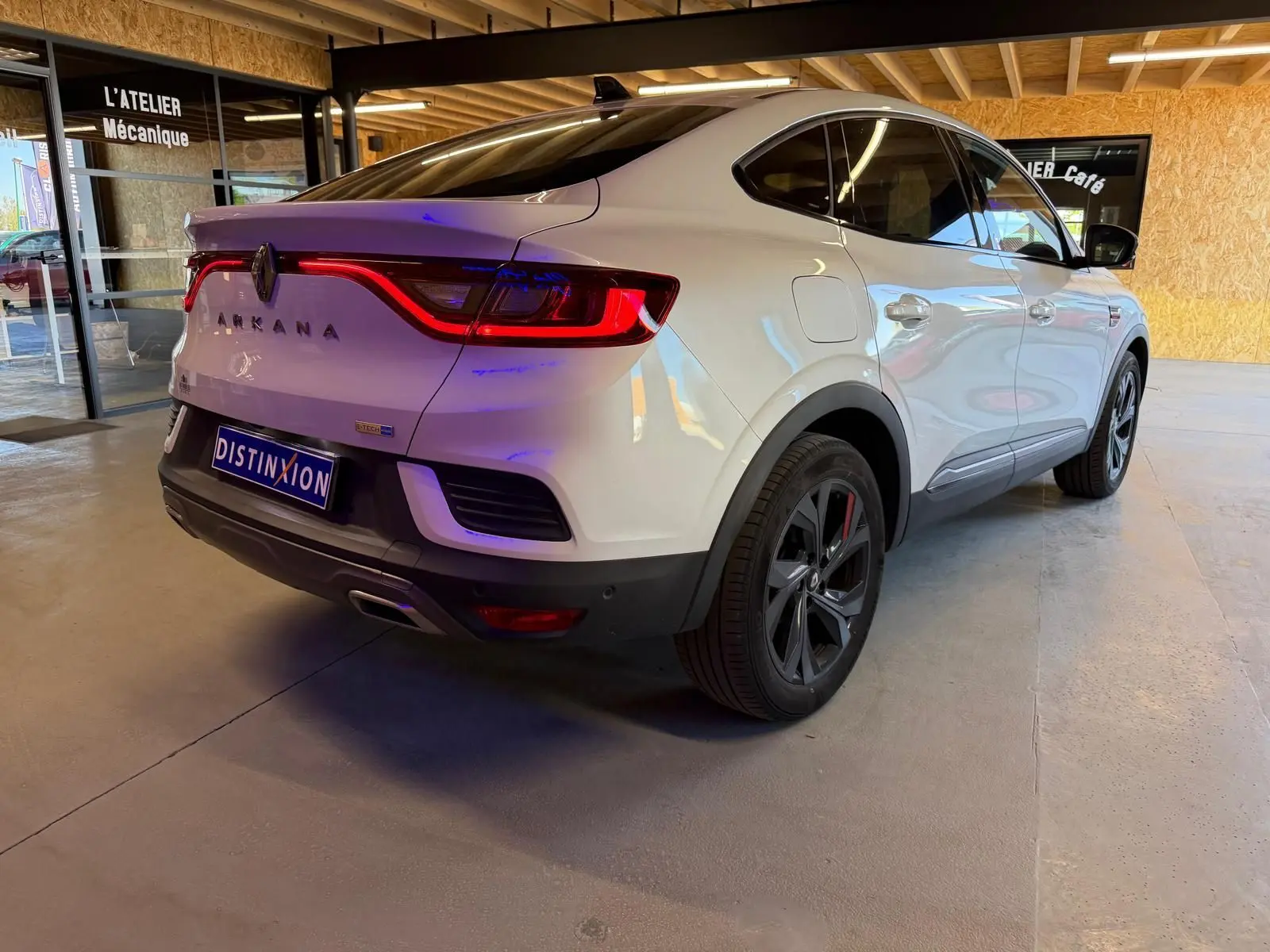 Vue 3/4 arrière droite d'une Renault Arkana blanc nacré avec feux arrière allumés et jantes alu noires.