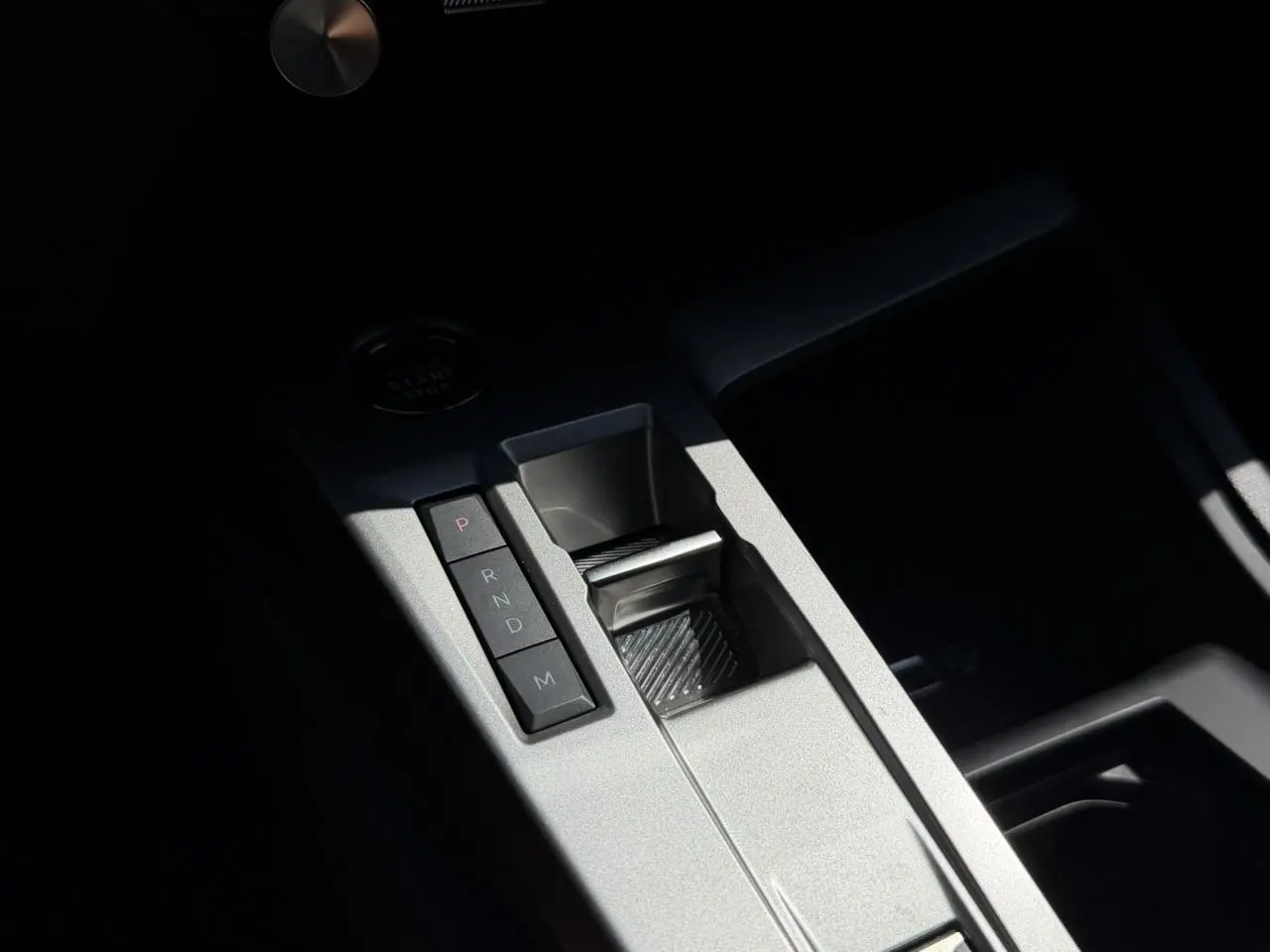 Gros plan sur la console centrale grise de la Peugeot 308 Hybrid 145, avec sélecteur de boîte auto et bouton start/stop.