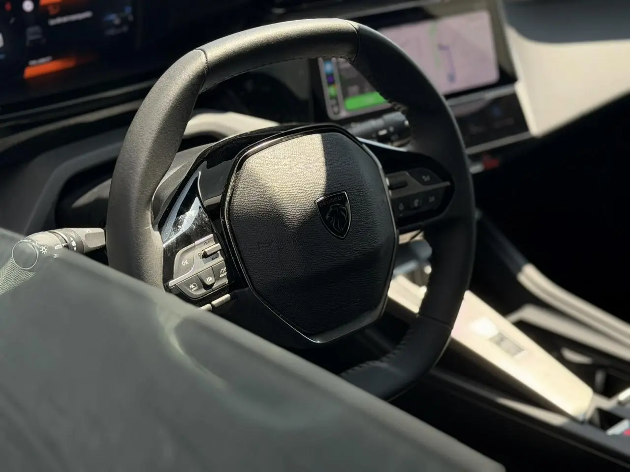 Intérieur de Peugeot 308 Hybrid 145, vue rapprochée du volant cuir noir avec commandes intégrées et tableau de bord digital.