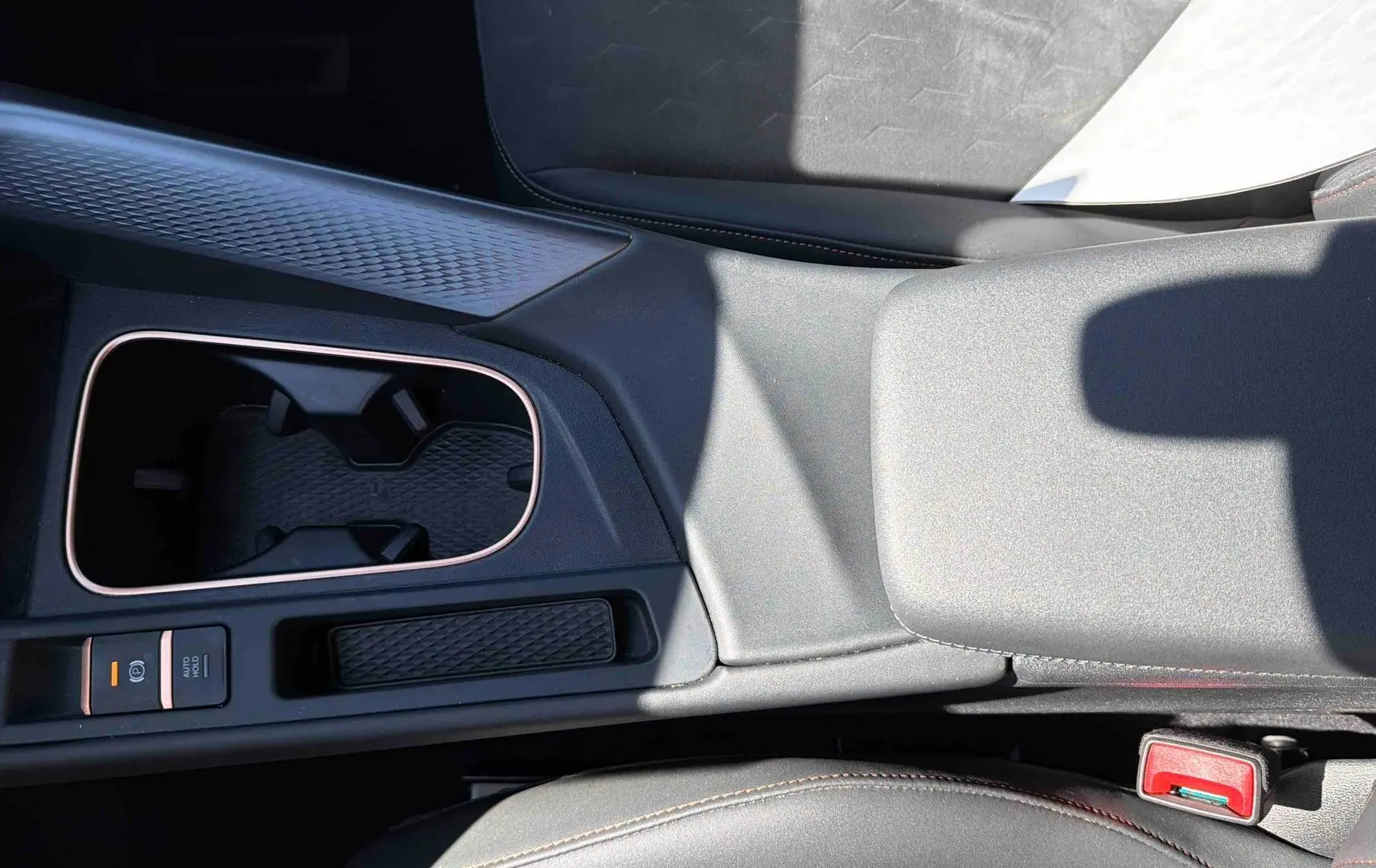 Vue rapprochée de la console centrale grise du CUPRA TERRAMAR 1.5 eHybrid avec porte-gobelets et frein à main électrique.