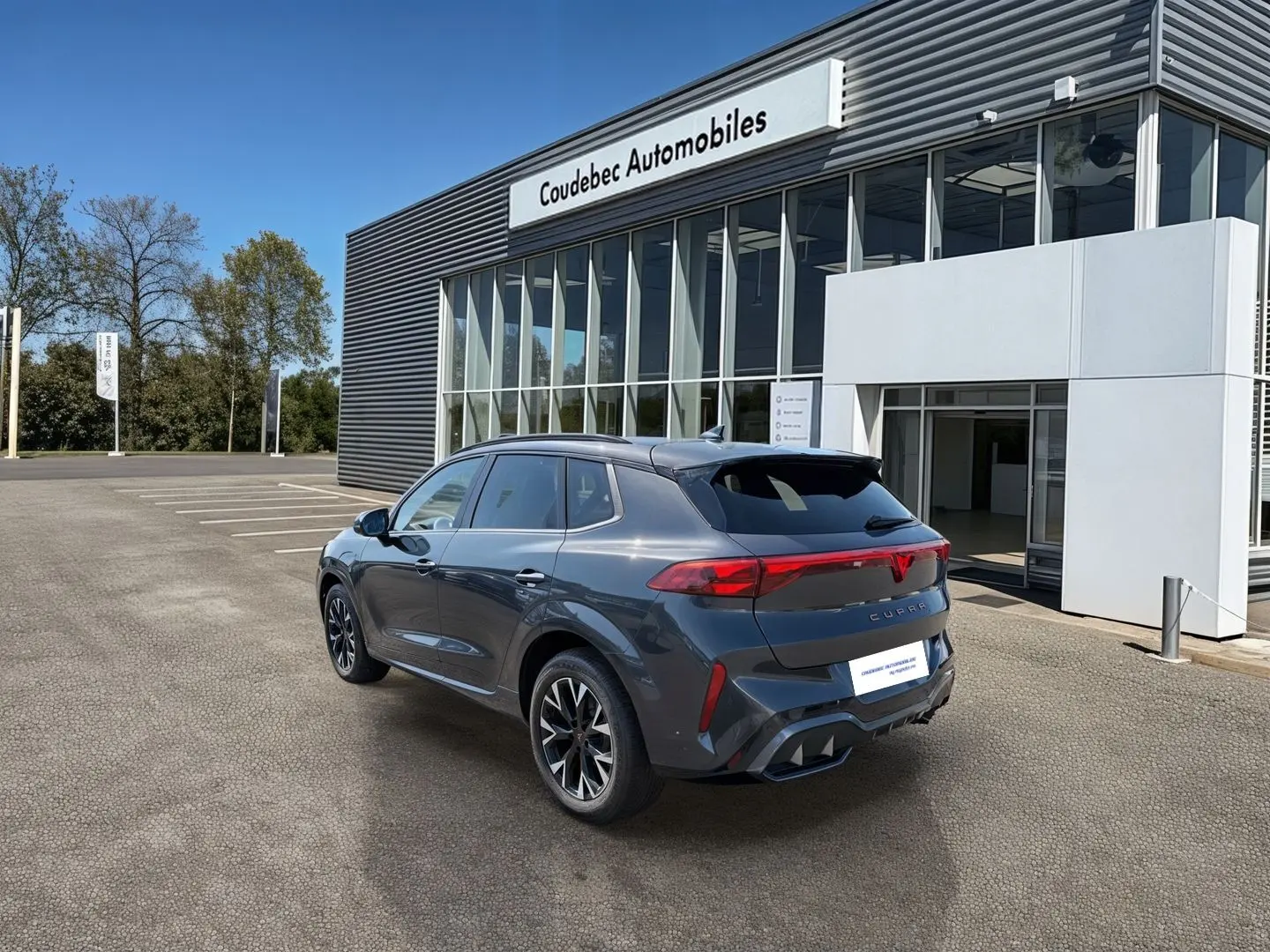 Vue 3/4 arrière droite d’un CUPRA TERRAMAR gris avec jantes 18’’ Atomic anthracites devant un concessionnaire.