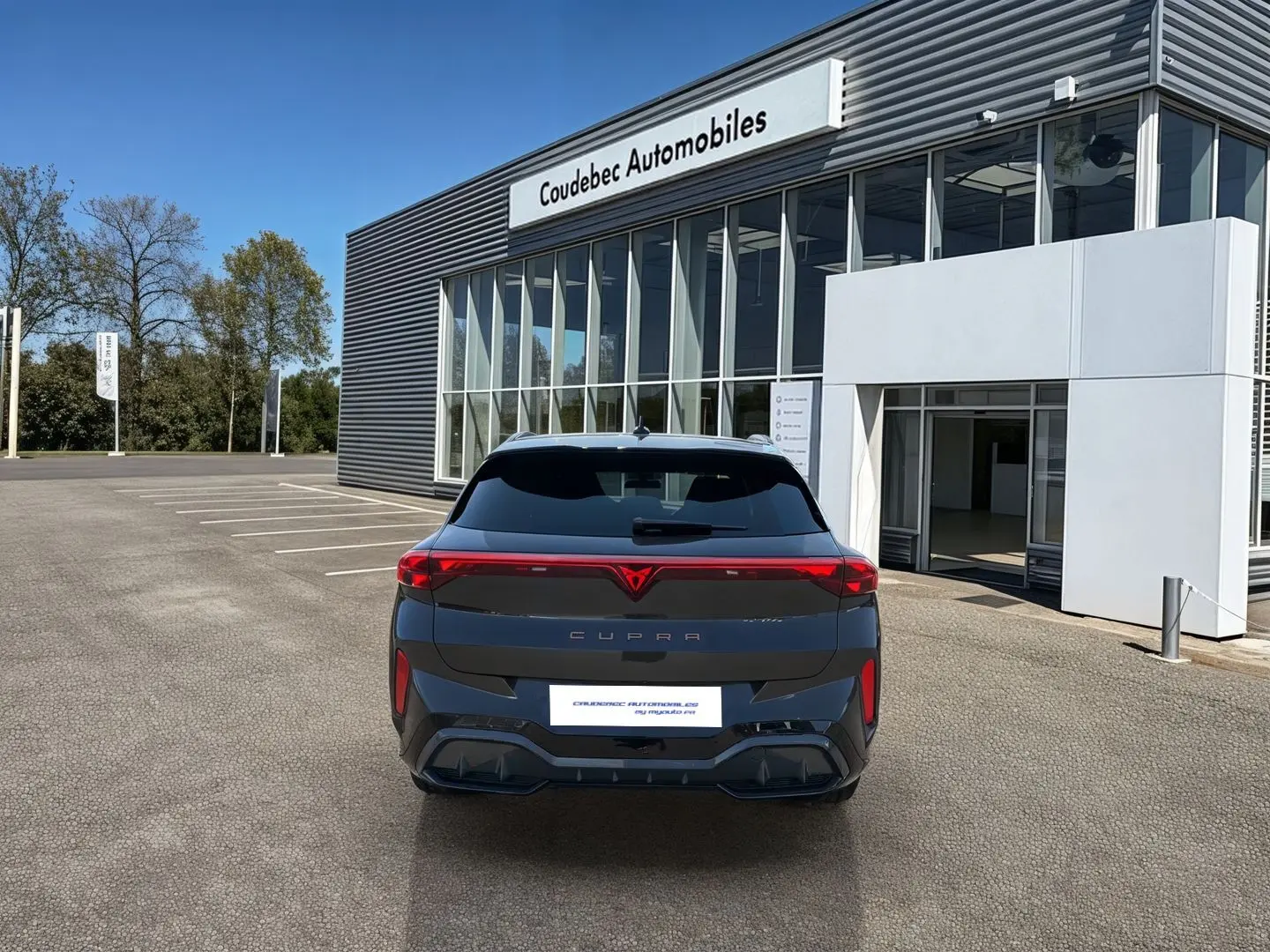 Vue arrière d'une CUPRA Terramar grise 2025 stationnée devant un bâtiment moderne de concession.