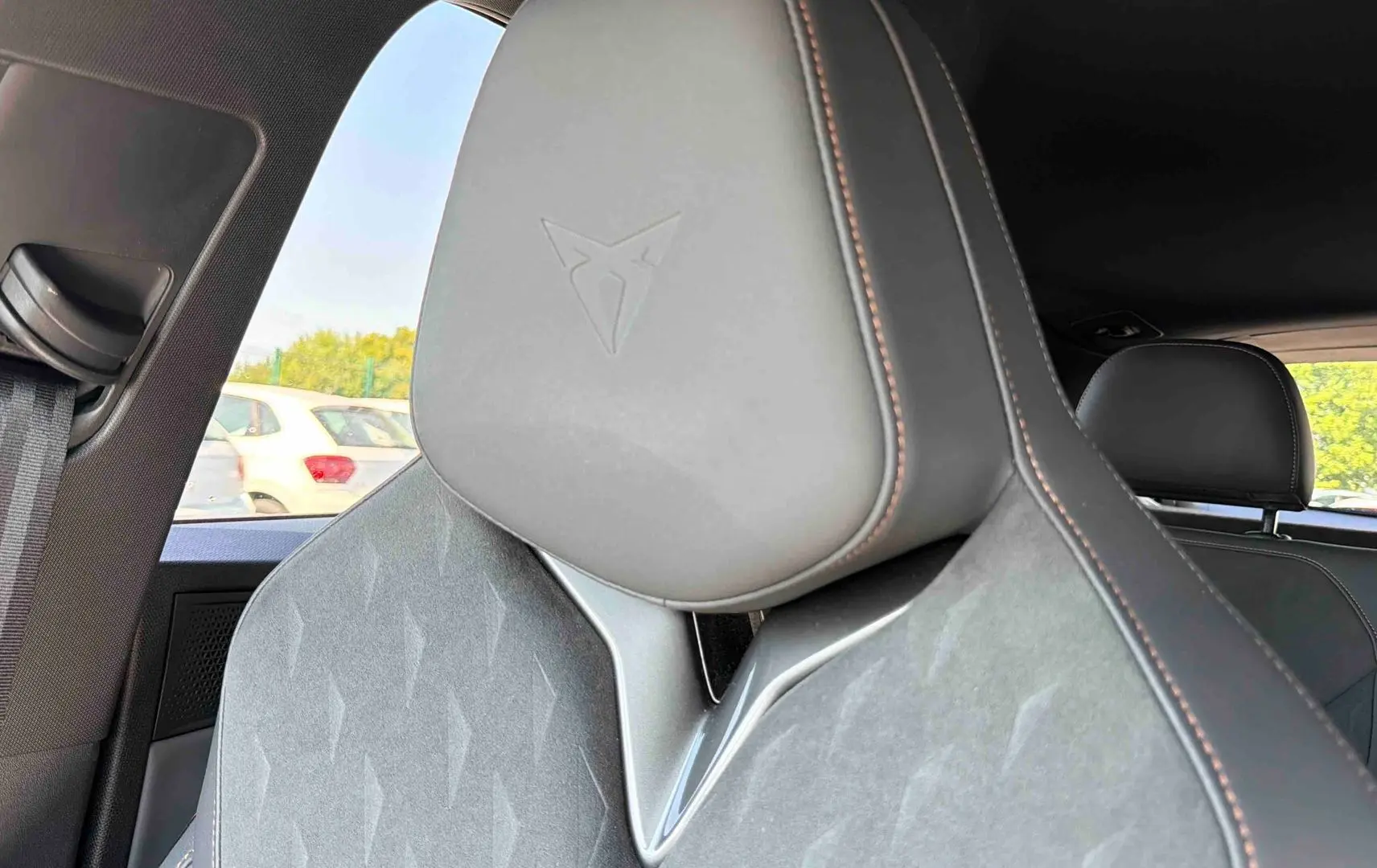Gros plan sur l'appui-tête gris avec logo Cupra embossé, siège avant en cuir et tissu, intérieur du véhicule visible.