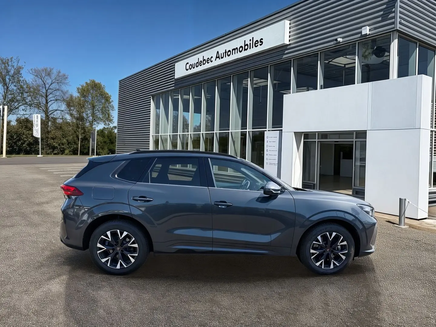 Vue latérale droite du CUPRA TERRAMAR gris 2025 avec jantes 18'' Atomic anthracites devant un concessionnaire.