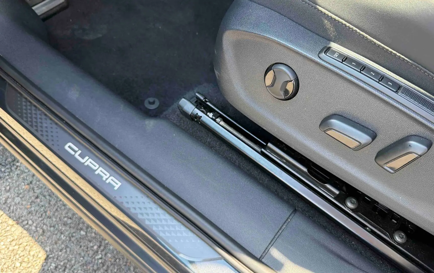 Gros plan sur le réglage électrique du siège avant droit et la plaque de seuil de porte CUPRA grise.