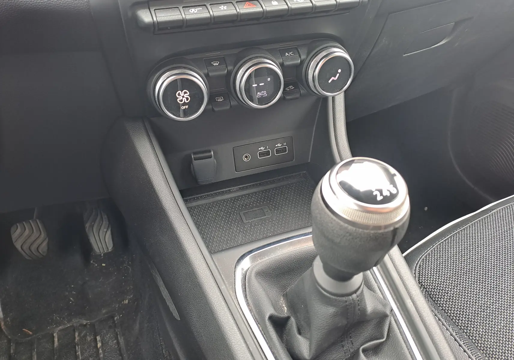 Gros plan sur la console centrale intérieure du Renault Captur 2024, mettant en valeur le levier de vitesses manuel et les commandes de climatisation.