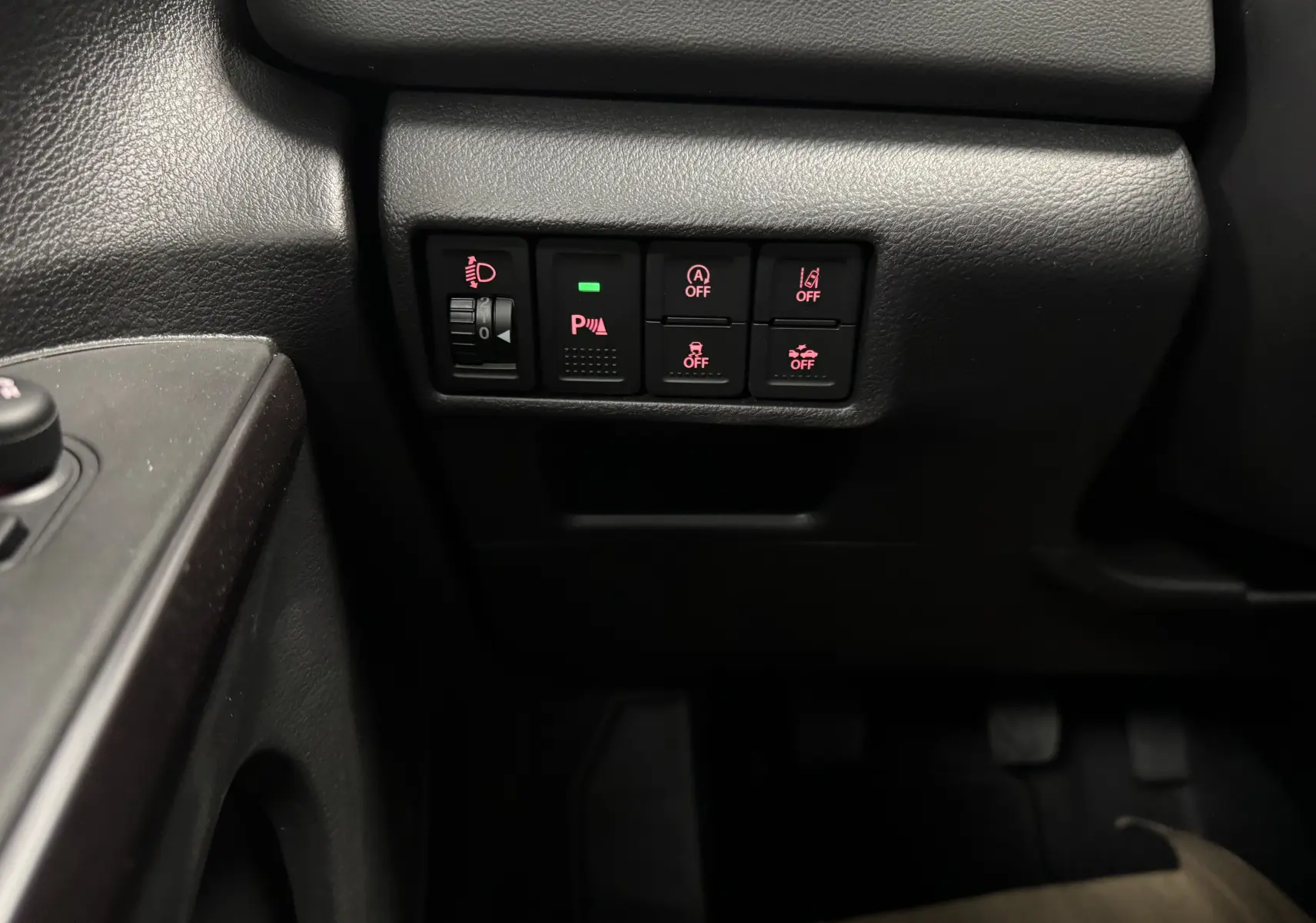 Gros plan sur les commandes de sécurité et d'assistance situées à gauche du conducteur dans le Suzuki S-Cross blanc 2025.