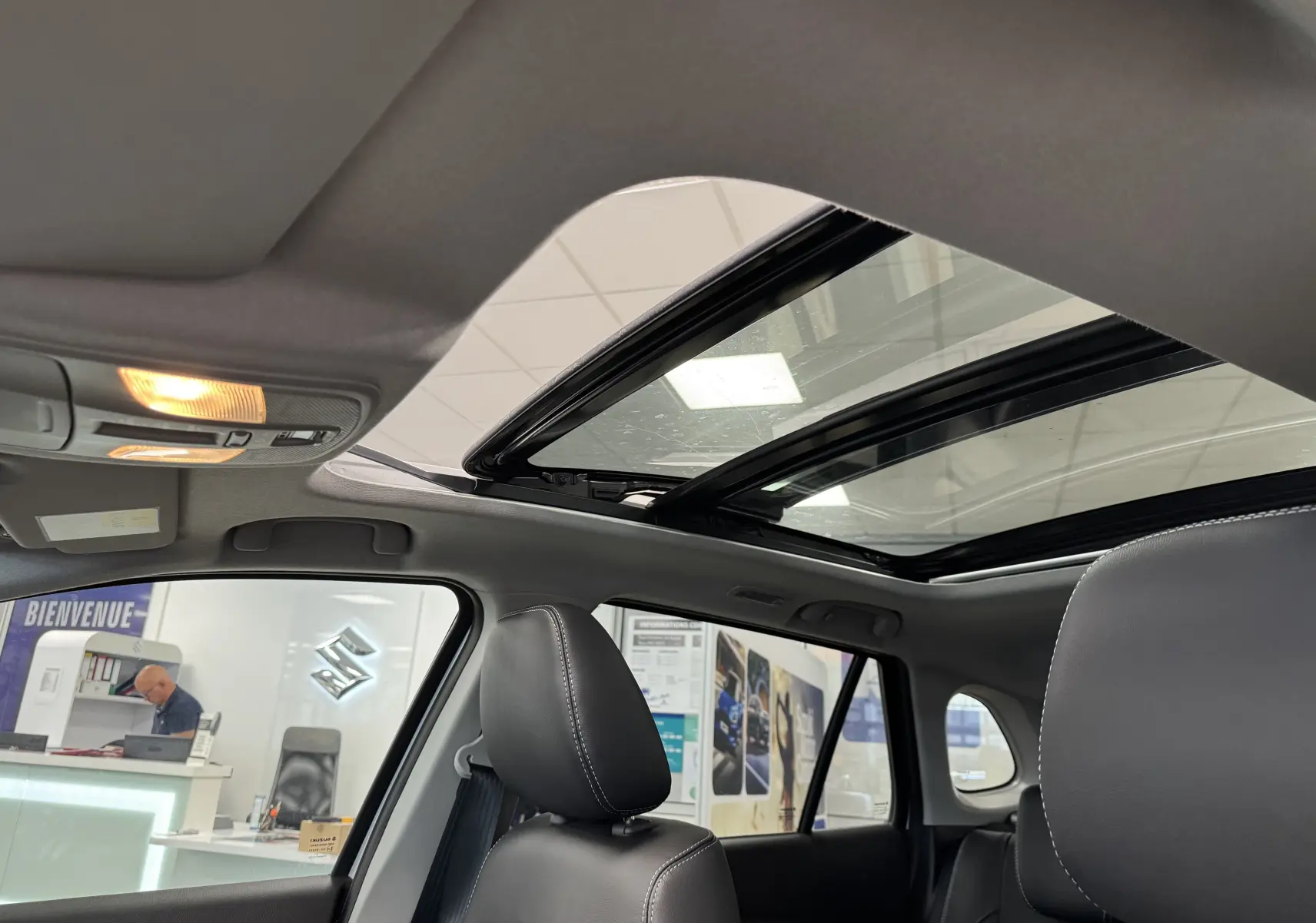 Intérieur du Suzuki S-Cross blanc 2025, vue du toit ouvrant panoramique et des sièges avant en cuir noir.