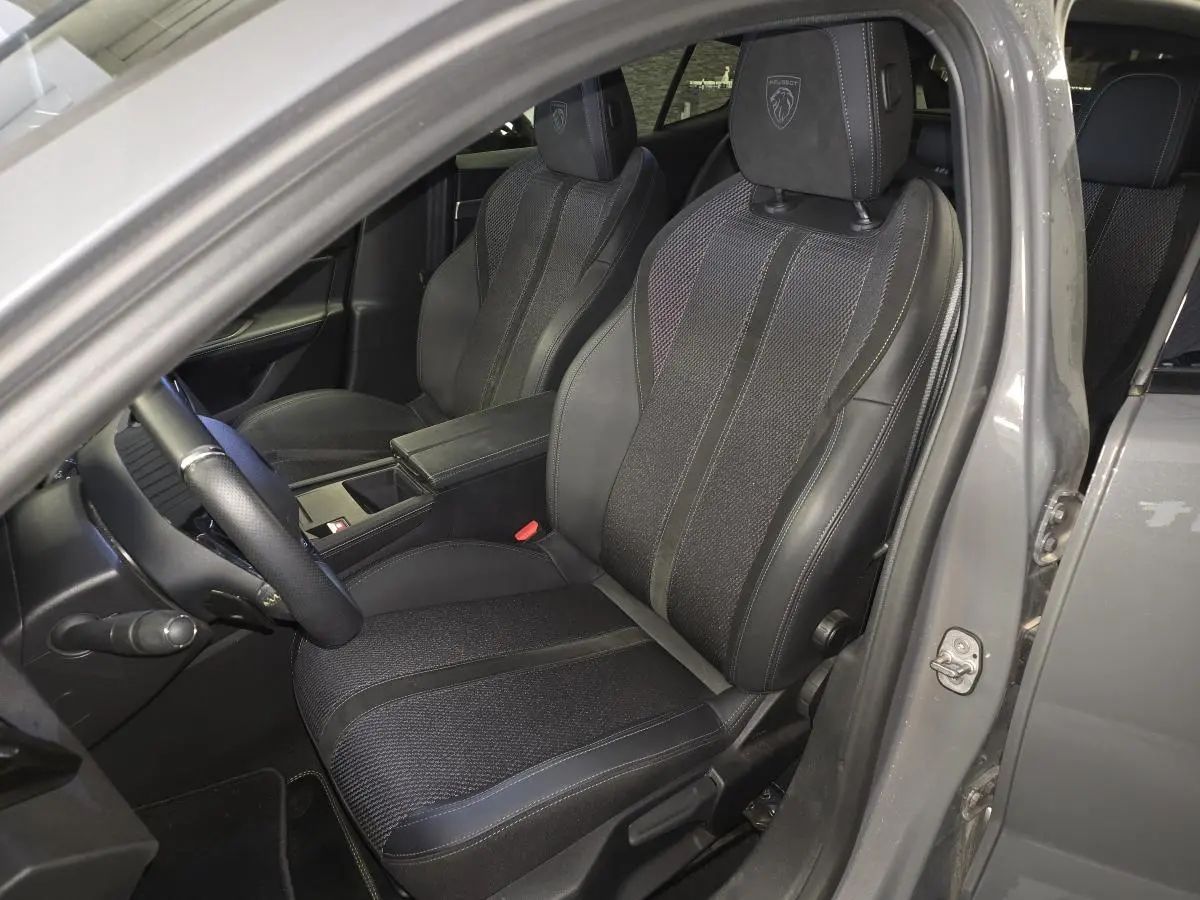 Vue intérieure côté conducteur du Peugeot 408 gris, mettant en valeur les sièges sport noirs avec logo Peugeot brodé sur les appuis-tête.